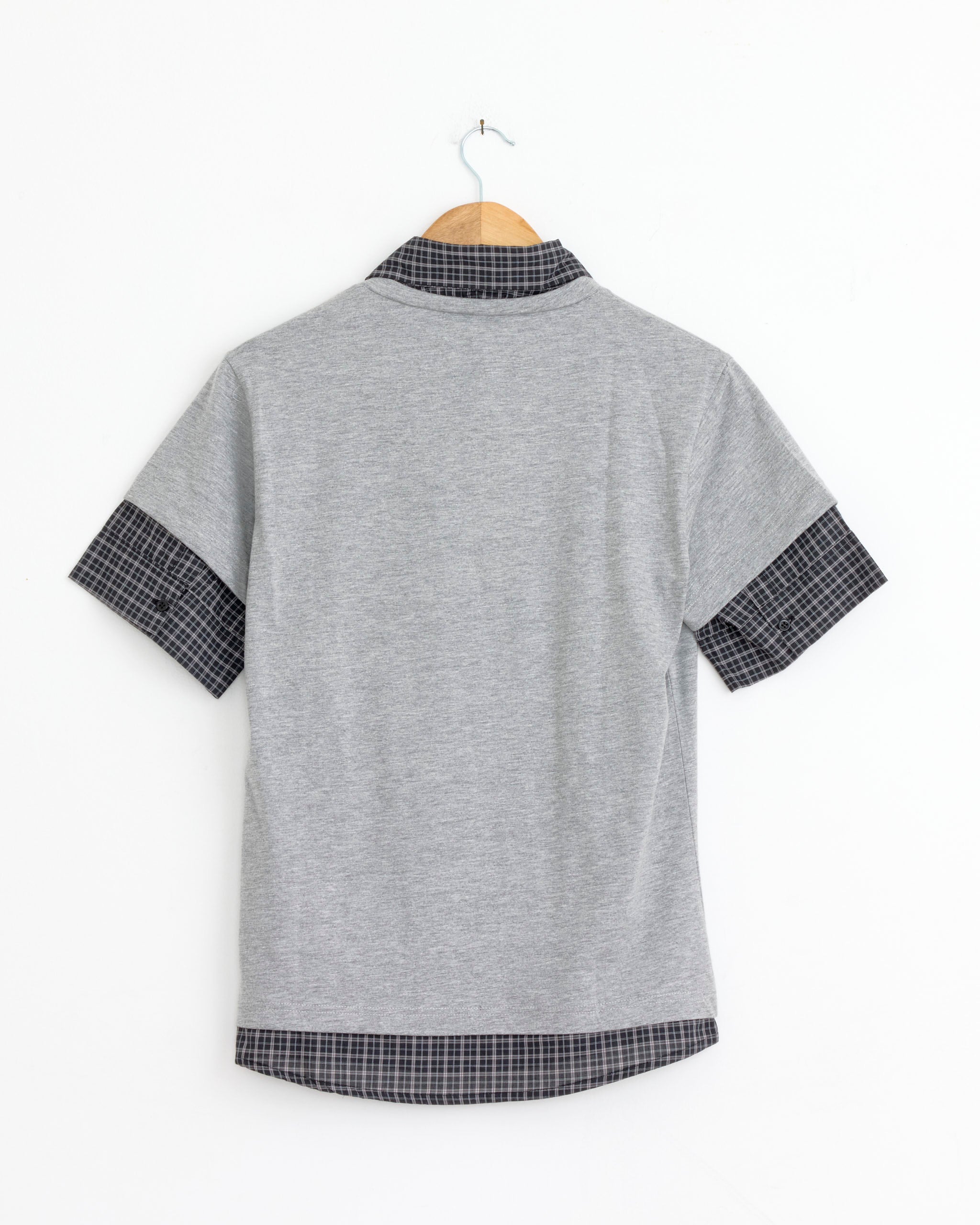 The Gimaguas Mauri Polo in Grey, an oversized unisex shirt with black and gray checkered collar, cuffs, and hem, is shown from the back on a wooden hanger against a white background.