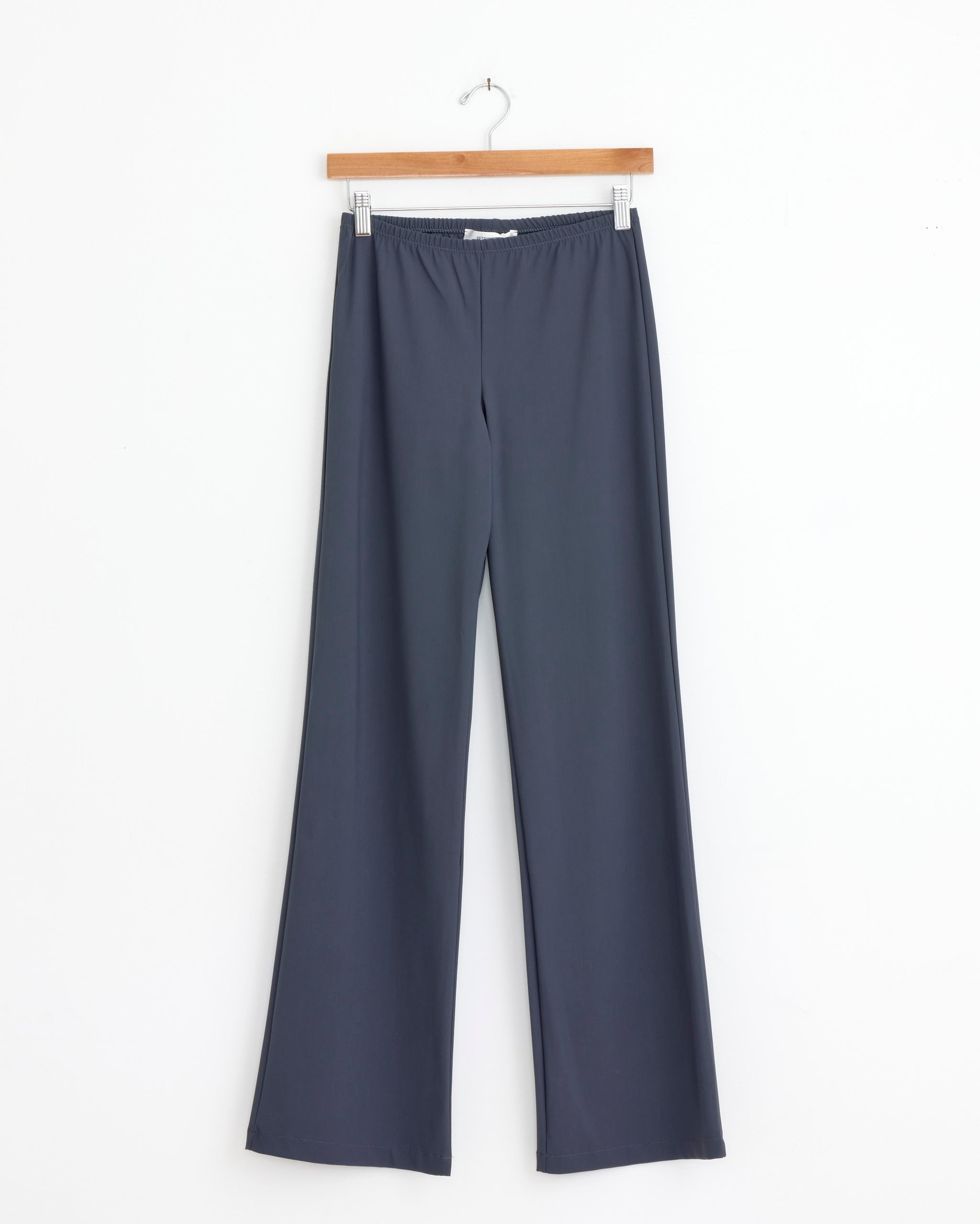 The Gimaguas Lula Trouser in Grey, featuring an elastic waistband and crafted from microfiber stretch fabric, hangs on a wooden hanger against a plain white background.