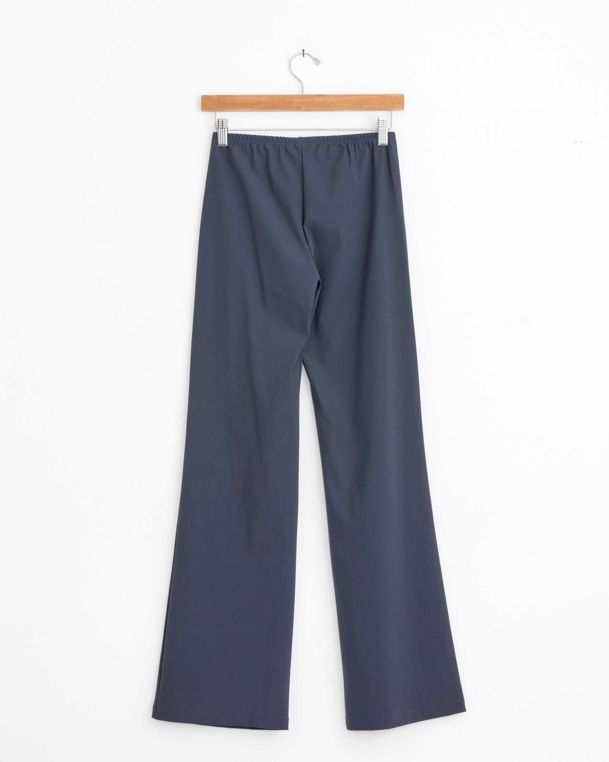 The Lula Trouser in Grey by Gimaguas, featuring wide legs and an elastic waistband in microfiber stretch fabric, hangs on a wooden hanger against a plain white background.