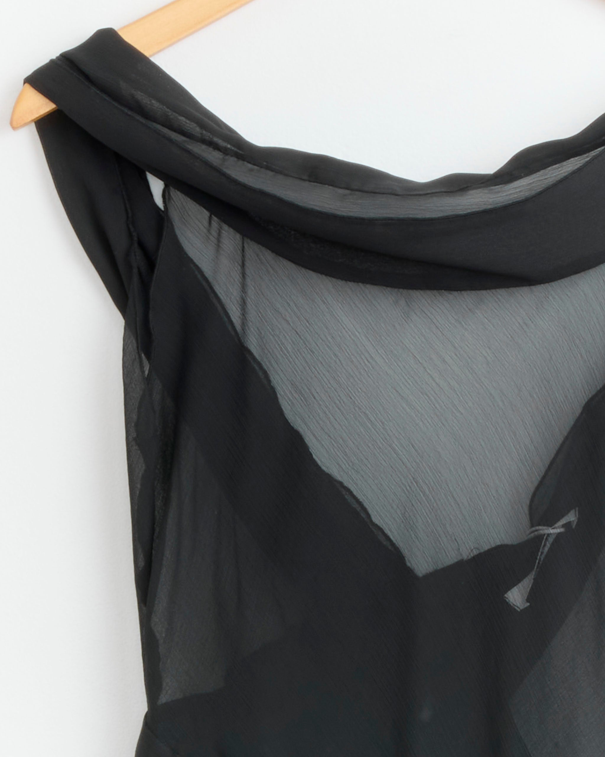 Close-up of the Gimaguas Boa Mini Dress in Black, a sheer chiffon off-shoulder mini dress, hanging on a wooden hanger against a white background.