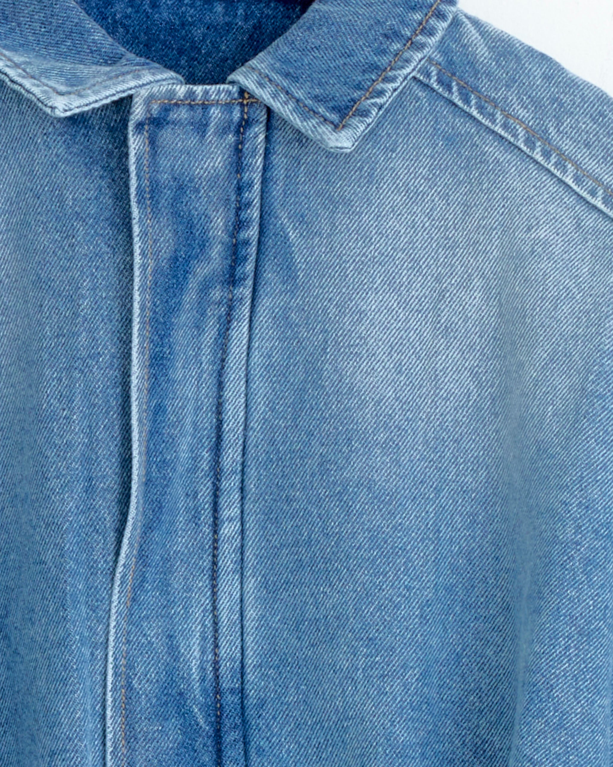 Close-up of the Gimaguas Mila Jacket in Blue Medium, highlighting the cotton fabric, collar, shoulder seam, and front placket with visible stitching details.