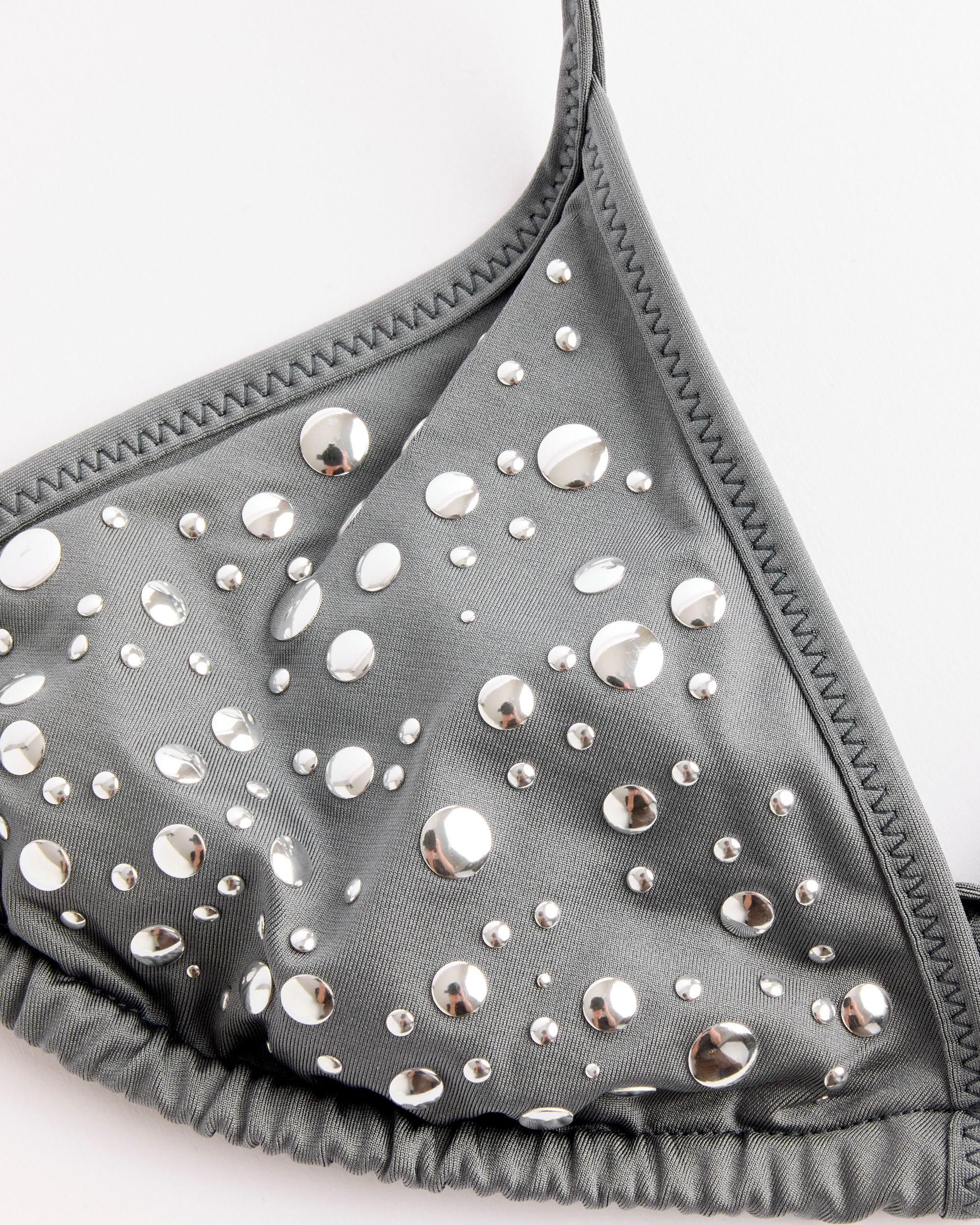 Close-up of the Gimaguas Gaia Bikini Top in Grey—a satin triangle swim top with round silver studs and metallic details, displayed against a white background.