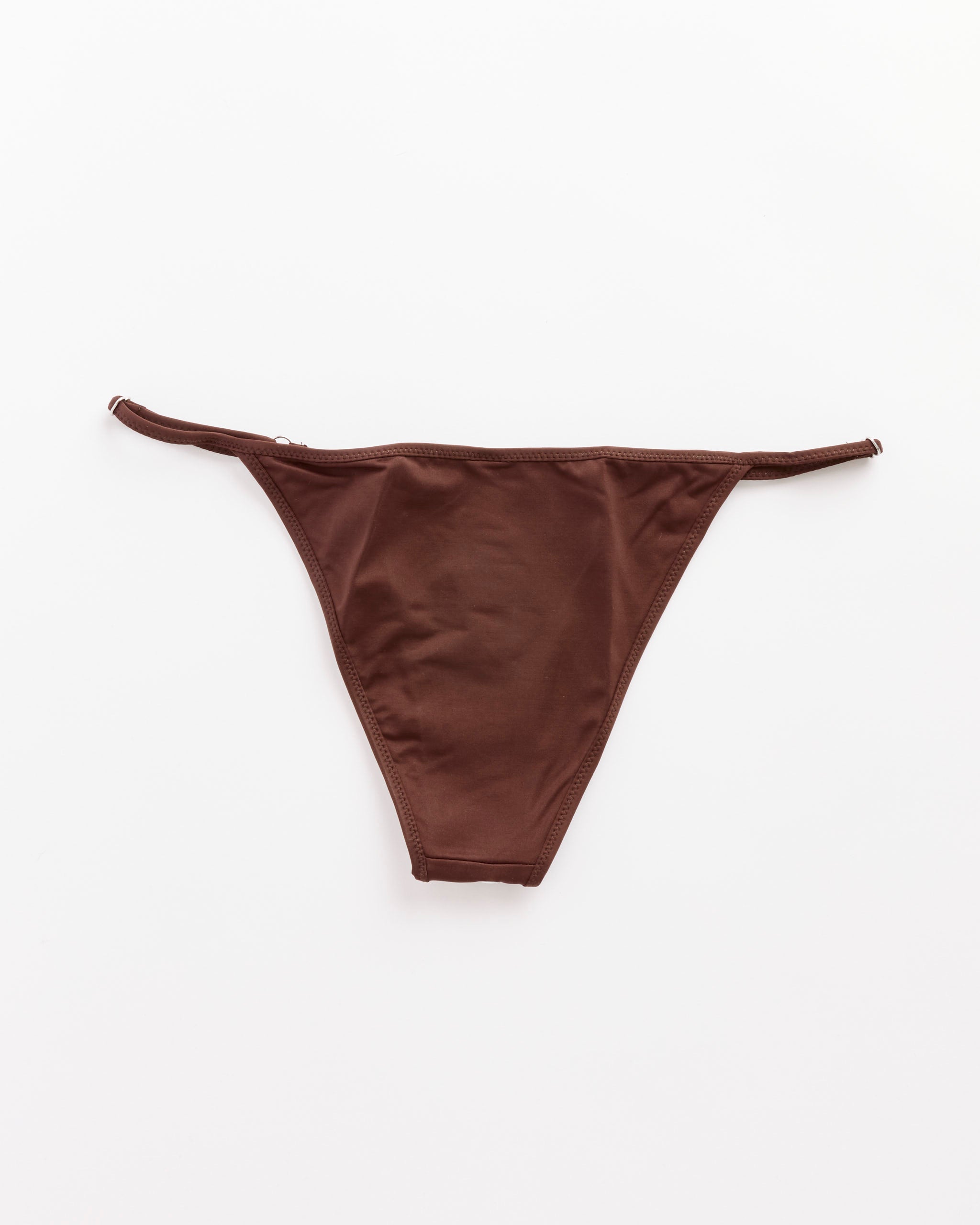The Emily Bikini Bottom in Brown by Gimaguas is a low-rise thong with thin, adjustable side straps, shown laid flat on a white background.
