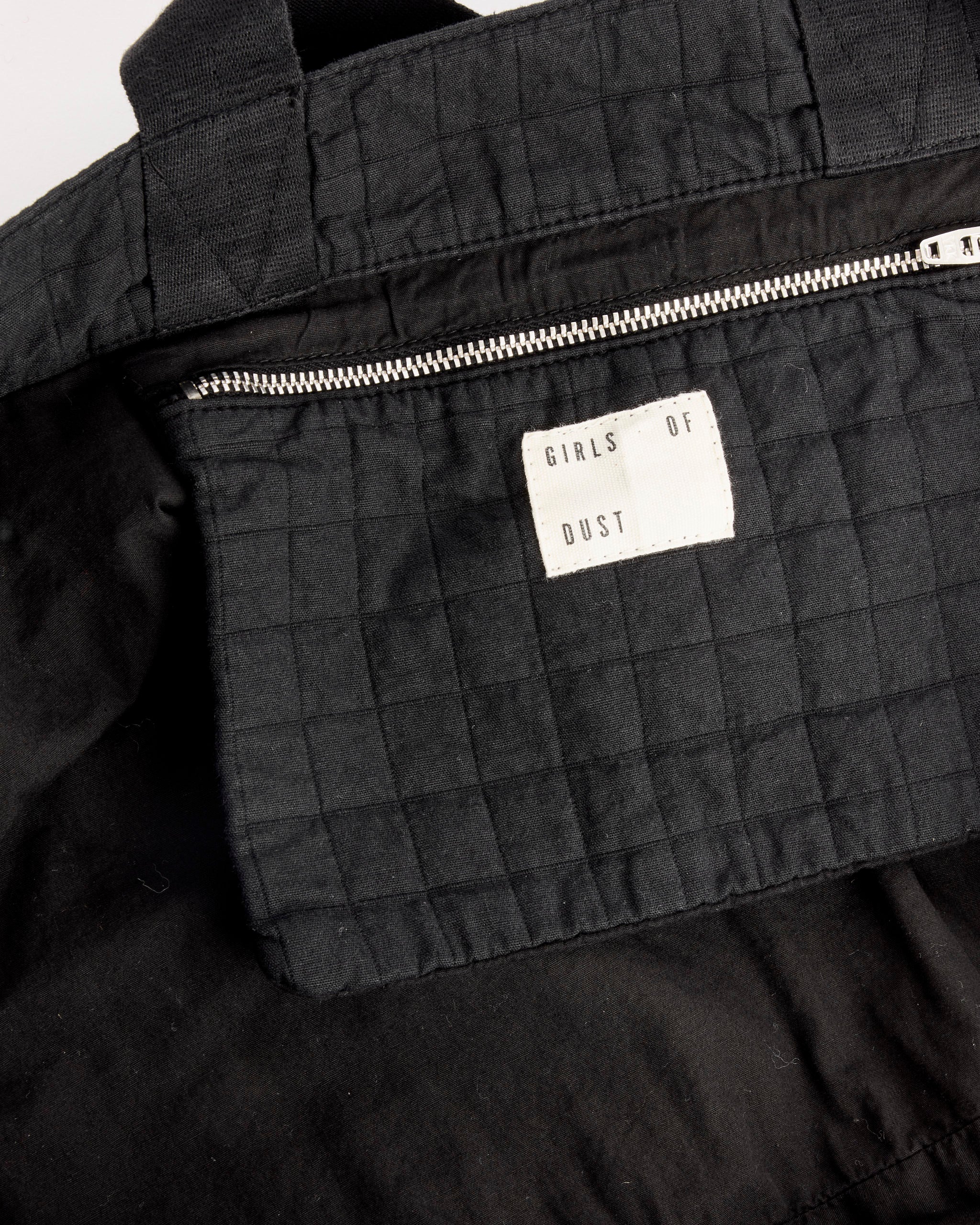 A close-up of the Girls of Dust Moon Bag in Black, made from quilted cotton with a silver zipper and a white interior label.