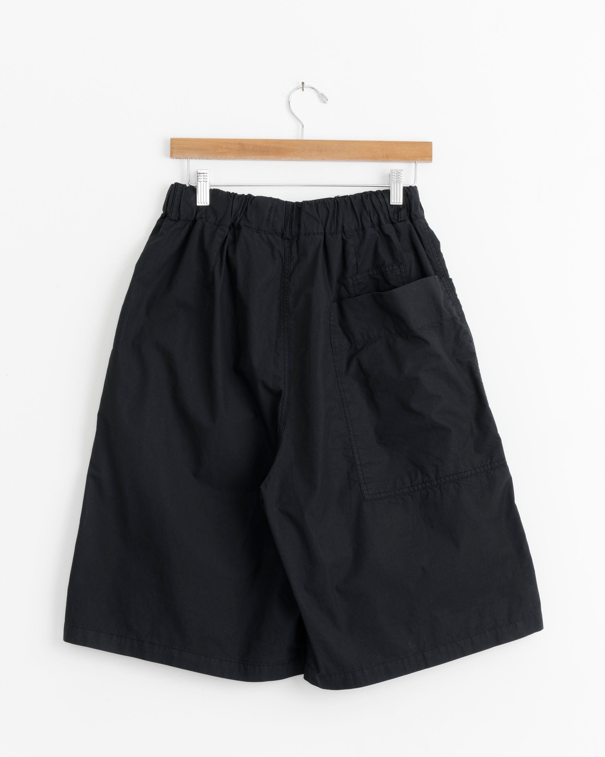 A pair of loose-fitting Bermuda Short in Midnight Blue by Girls of Dust, featuring a drawstring waist and large side pocket, hangs on a wooden hanger against a white background.