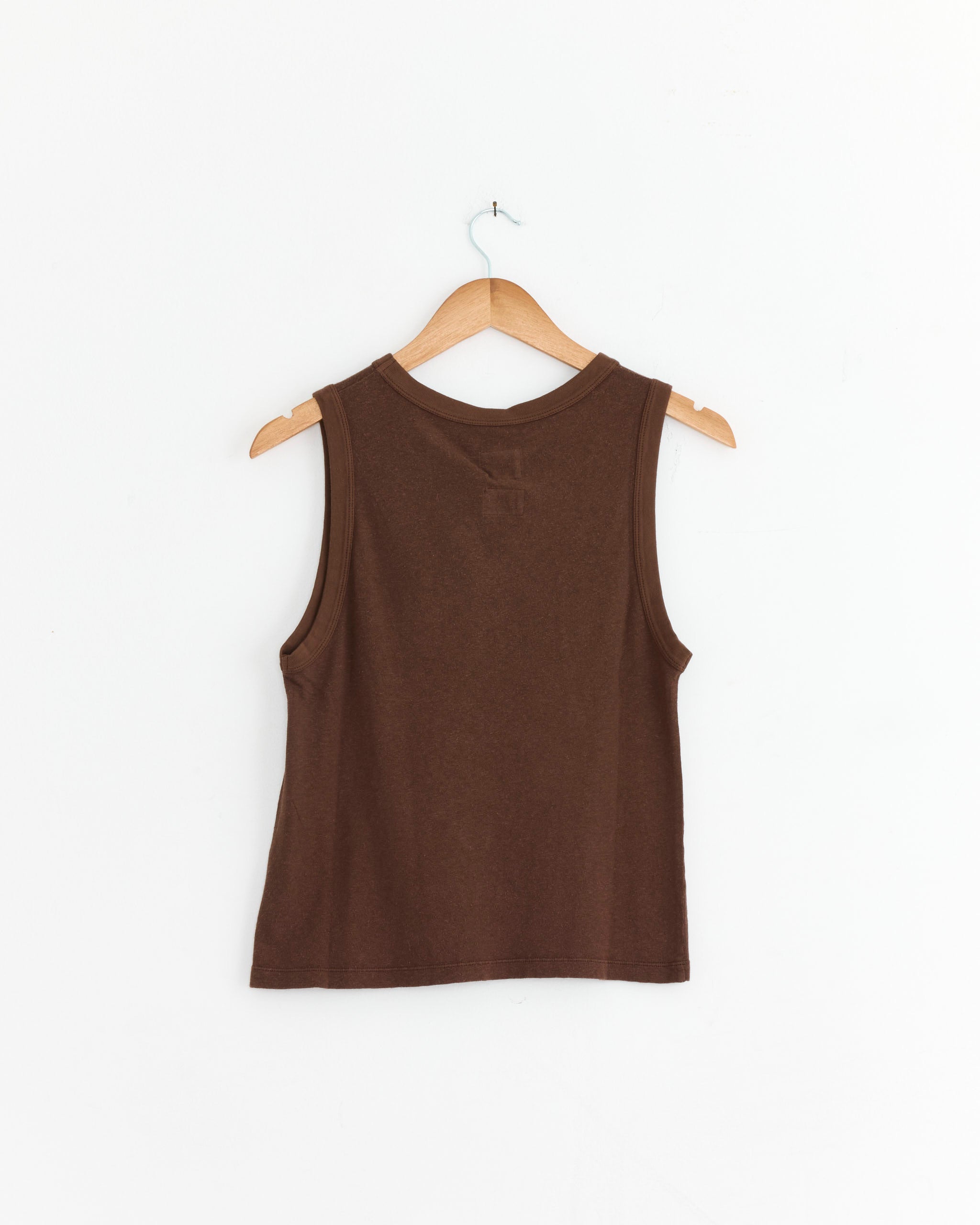 The Girls of Dust Johnny Tee in Aztek Brown, a women's sleeveless top made in Portugal, hangs on a wooden hanger with its back facing forward against a plain white background.