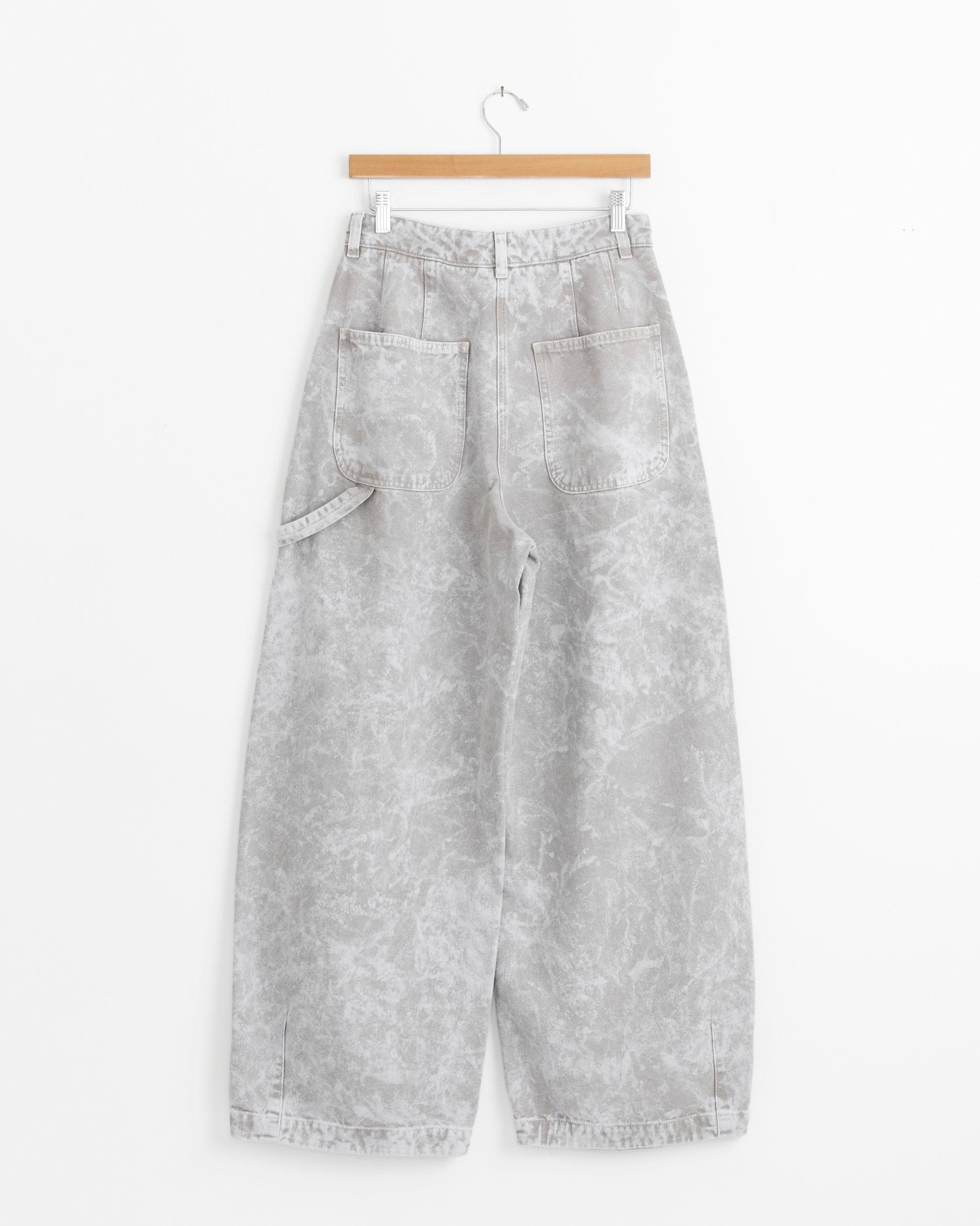 The Atlantide Chino in Marble by Girls of Dust features light gray, high-waisted, wide-leg jeans with a marbled pattern, two back pockets, and a side loop, displayed on a wooden hanger against a white background.