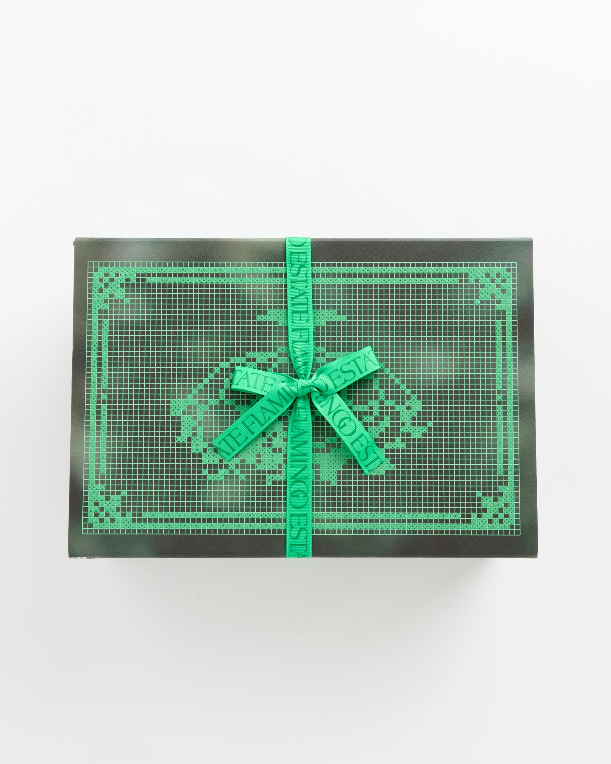 Flamingo Estate’s Jasmine Damask Rose Set comes in a rectangular green box with a decorative grid, tied with a matching ribbon bearing printed text—ideal for presenting a rich cream soap brick, displayed against a white background.