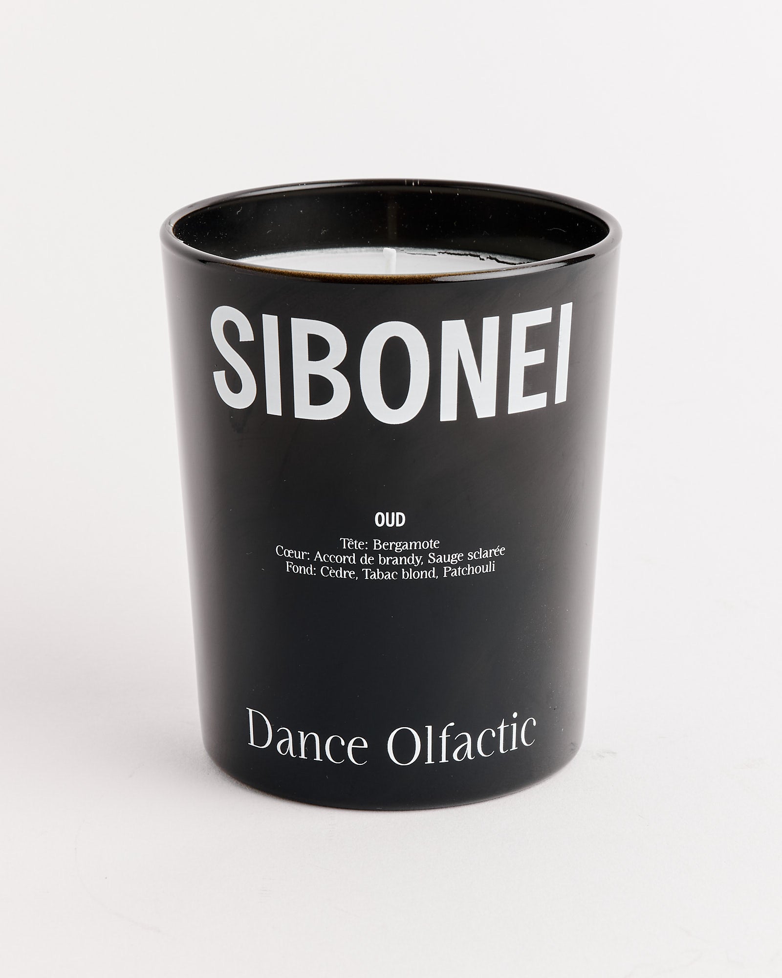 A black coconut wax candle from SIBONEI, labeled with white text listing oud, bergamot, cedar, and patchouli notes; "Dance Olfactic" appears at the bottom of the glass container.