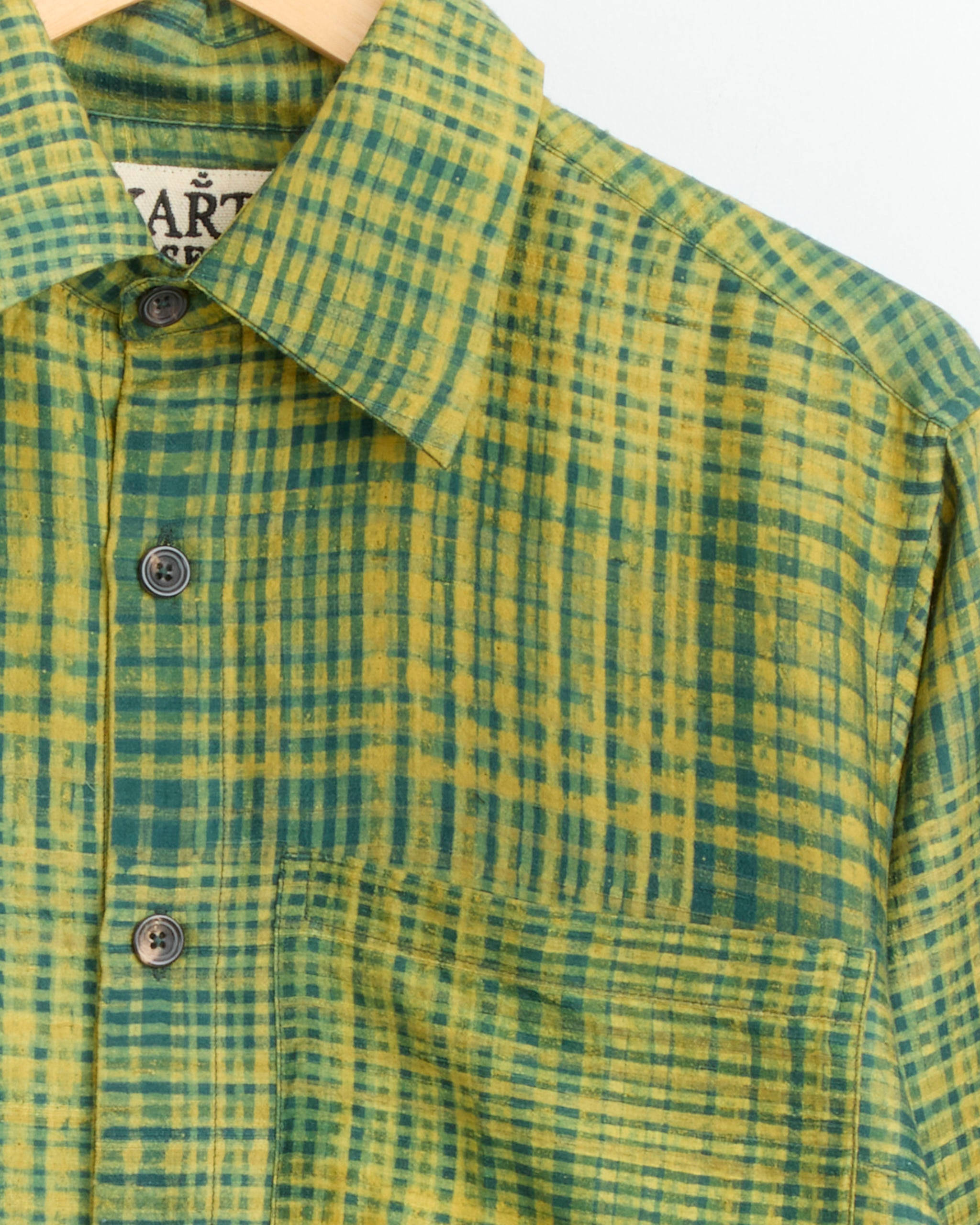 Close-up of the Kartik Research Pataudi Shirt in Green/Black/Moss, crafted from handwoven linen with a front pocket, displayed on a wooden hanger against a plain white background.