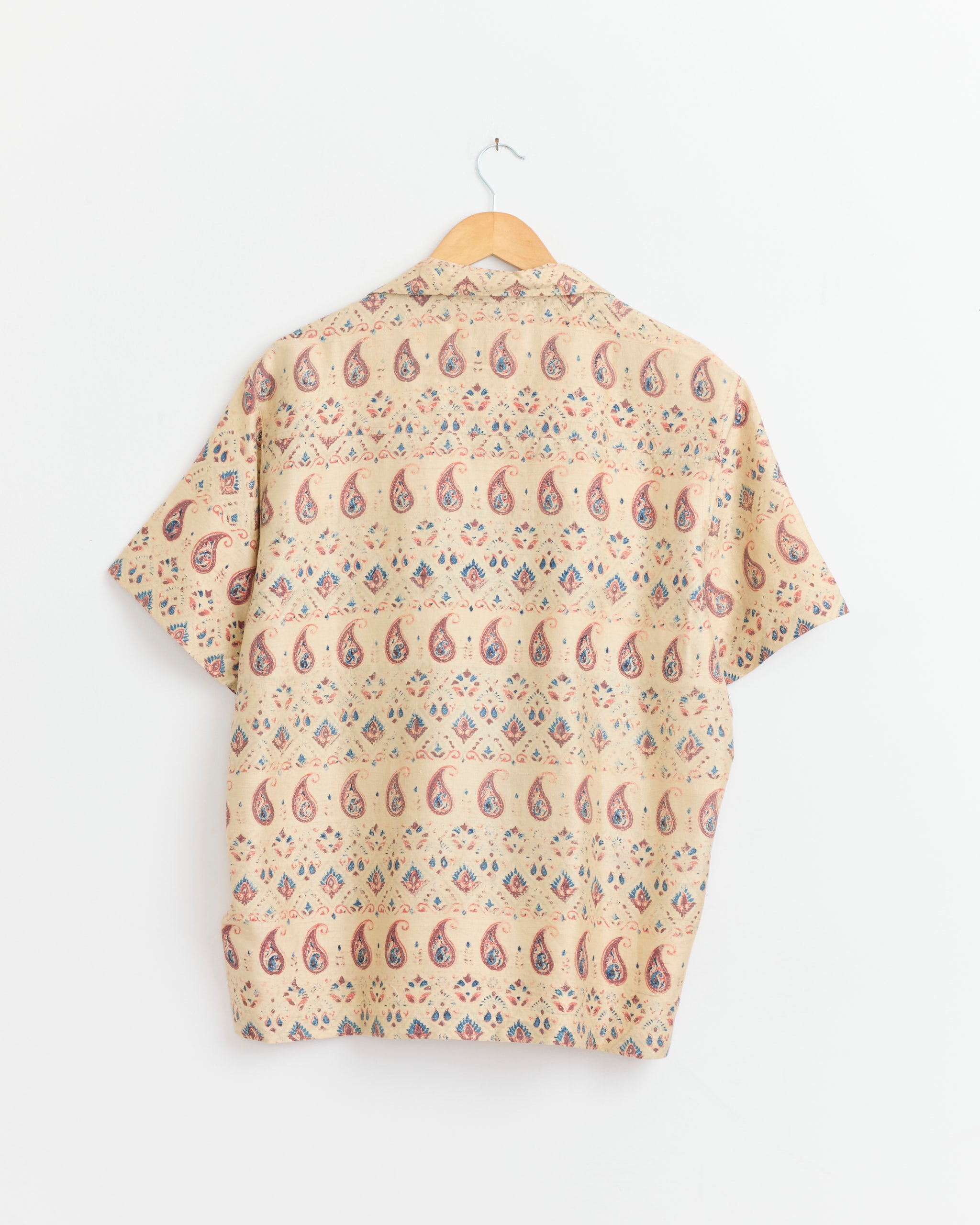 The Kartik Research Camp Shirt in Ecru/Orange/Indigo, featuring an Ajrakh-inspired paisley and diamond print, hangs on a wooden hanger against a white background.