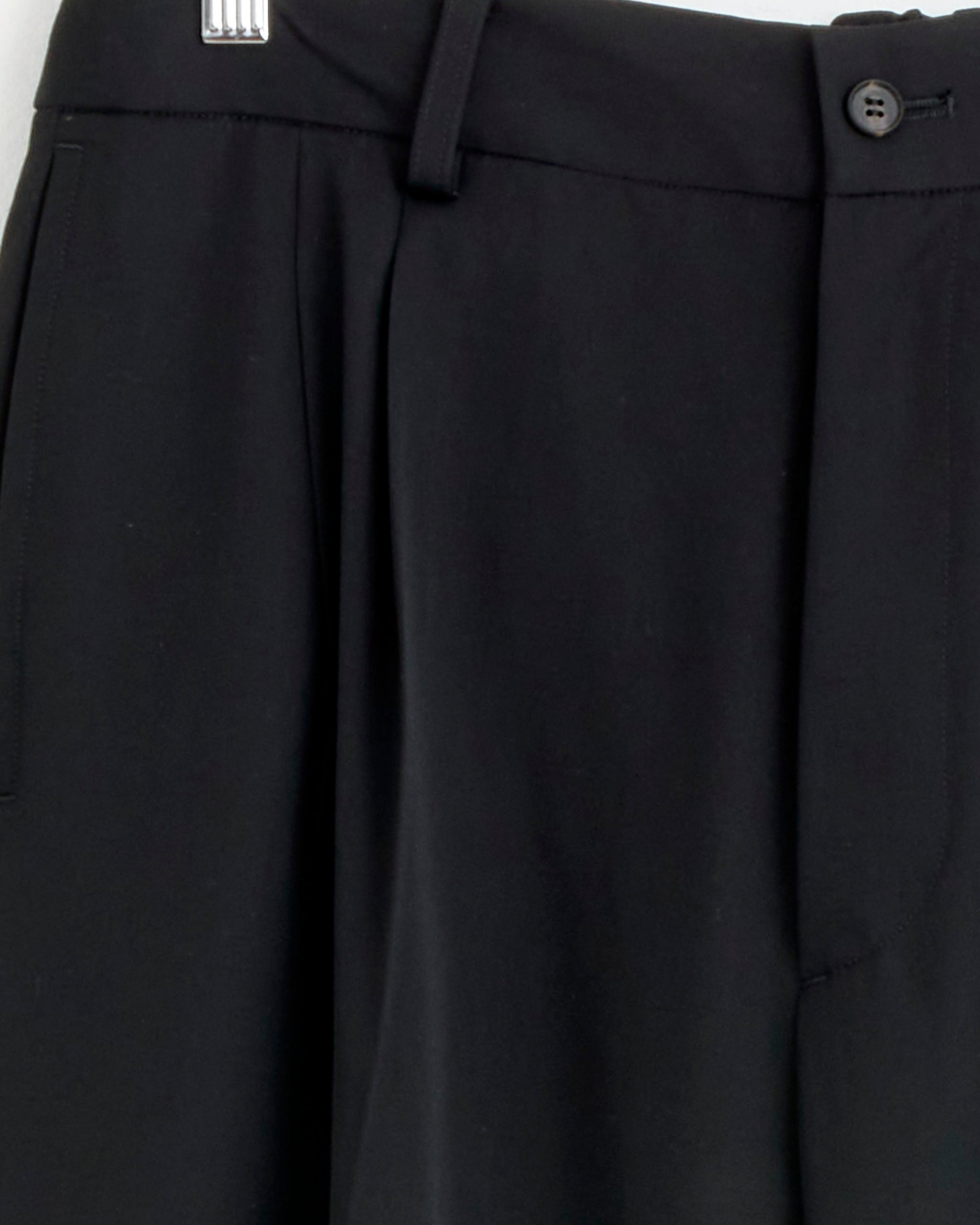 Close-up of the waistband and upper section of ssstein's The 1430 Two-Tuck Pant in Black, featuring a button closure, belt loops, and side pocket; crafted from wool in Japan and shown against a white background.