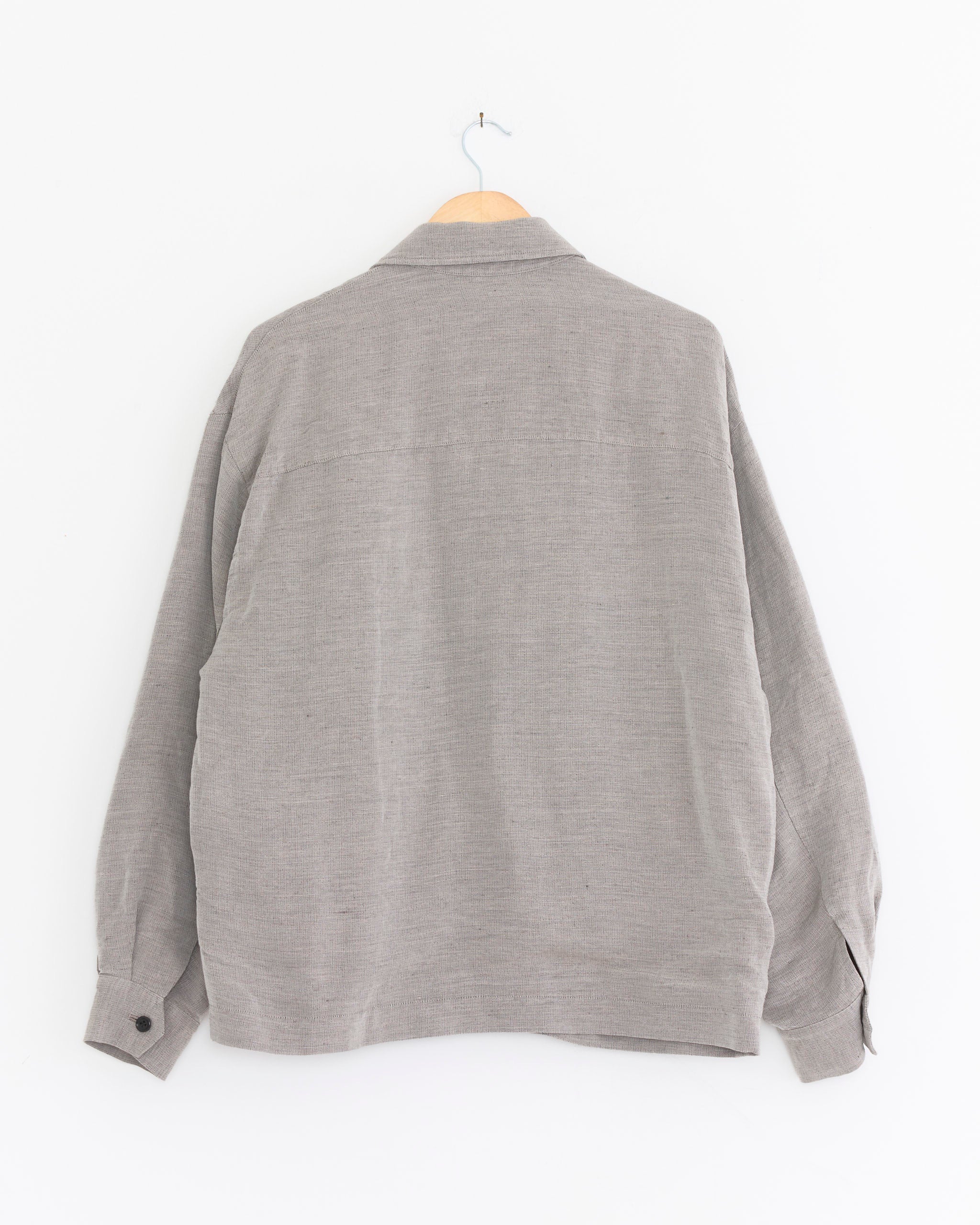 The Graphpaper Linen Cupronickel Hopsack Harrington Jacket in Taupe, inspired by classic Harrington style, is displayed from the back on a wooden hanger against a white wall.