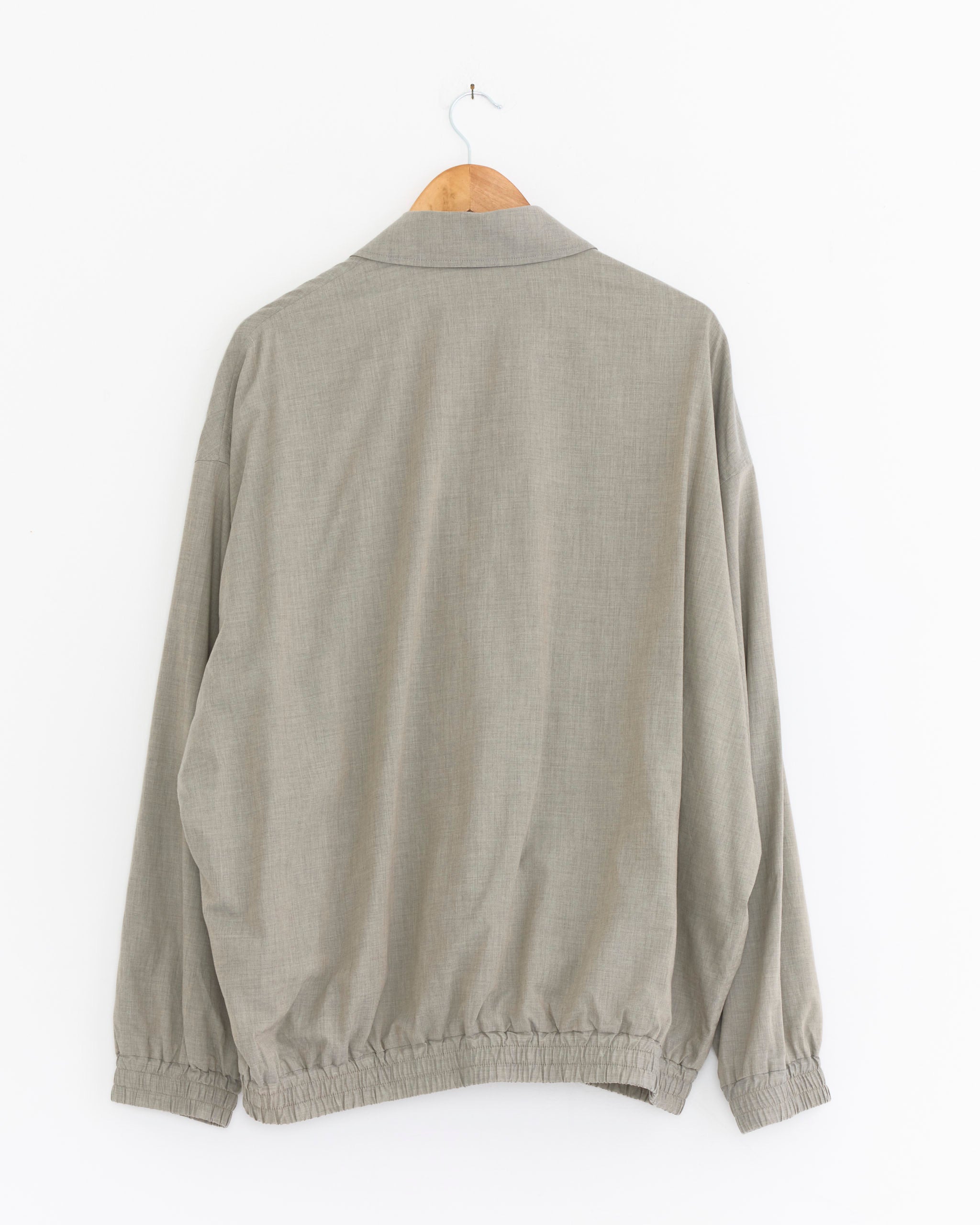 The Graphpaper Cotton Wool Poplin Oversized Blouson in grey hangs on a wooden hanger, back facing forward, against a white background. Made in Japan, it features an elastic waistband and cuffs.
