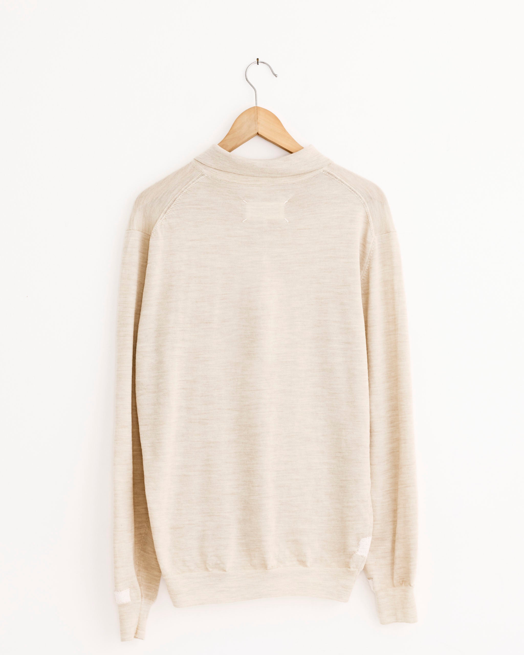 The Maison Margiela Polo Patchwork Shirt in Beige, with long sleeves and a knit wool-blend design, hangs on a wooden hanger against a plain white background, shown from the back.