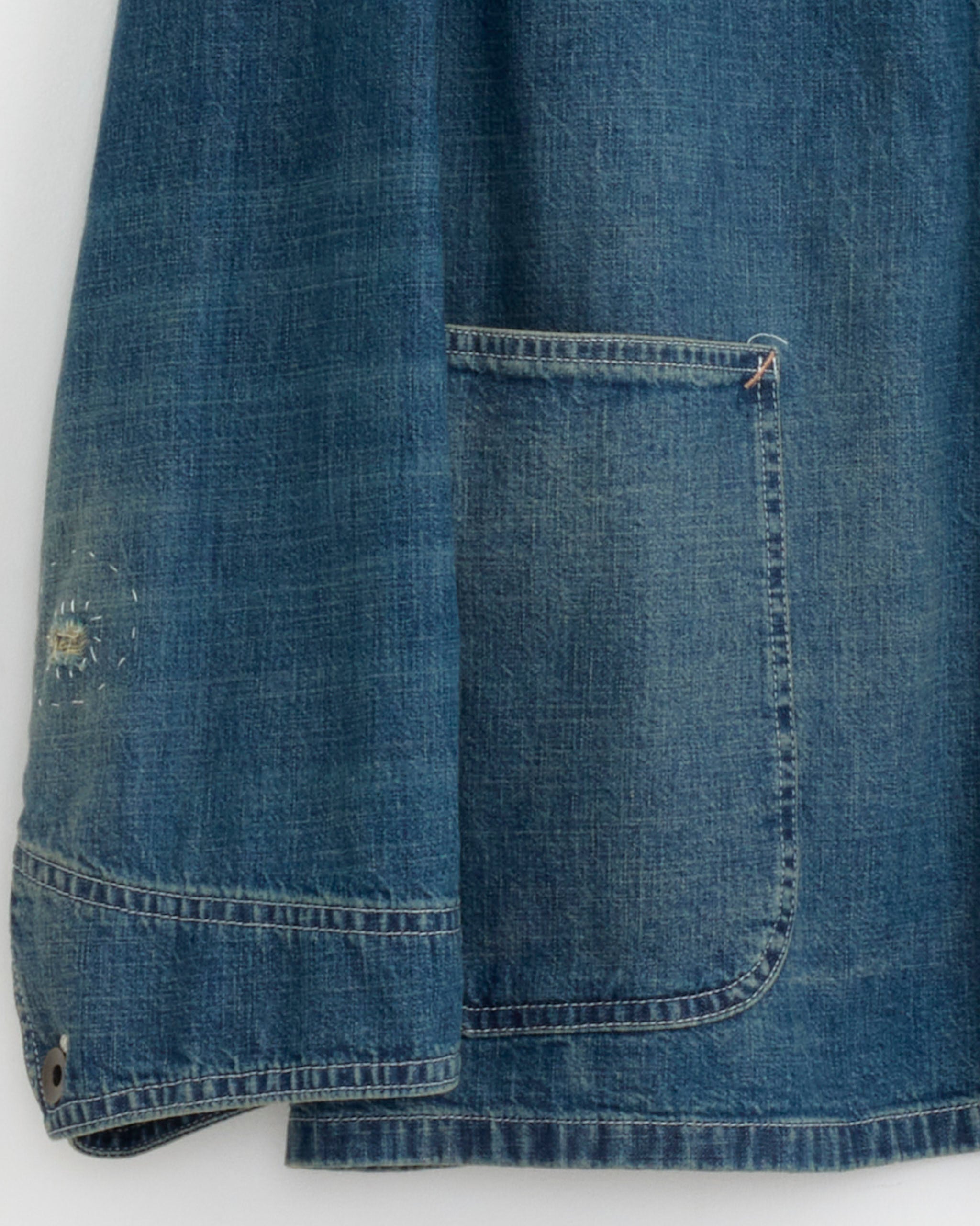 Close-up of the Maison Margiela Sports Jacket in Washed Blue, showing a worn, textured sleeve and front pocket with visible fading and a small patched hole near the cuff.
