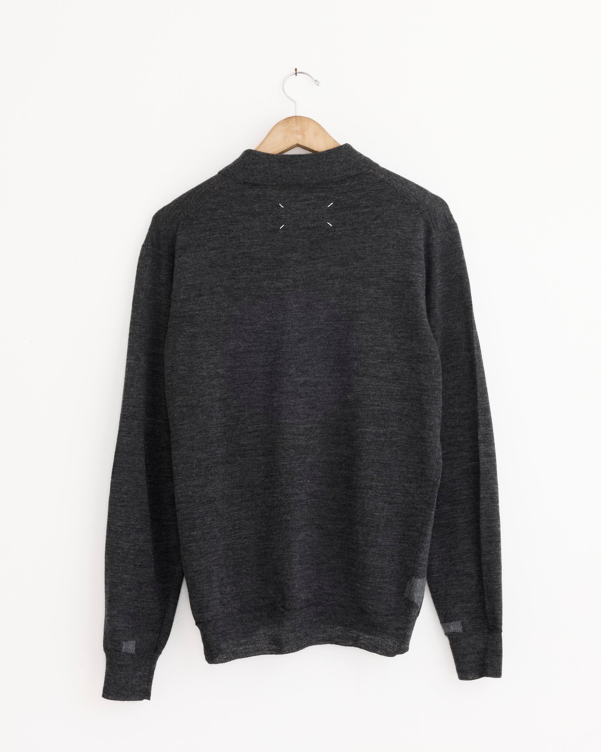 The Maison Margiela Polo Shirt in Medium Grey, a lightweight knit wool-blend, hangs on a wooden hanger against a white wall and is shown from the back with a simple, logo-free design.