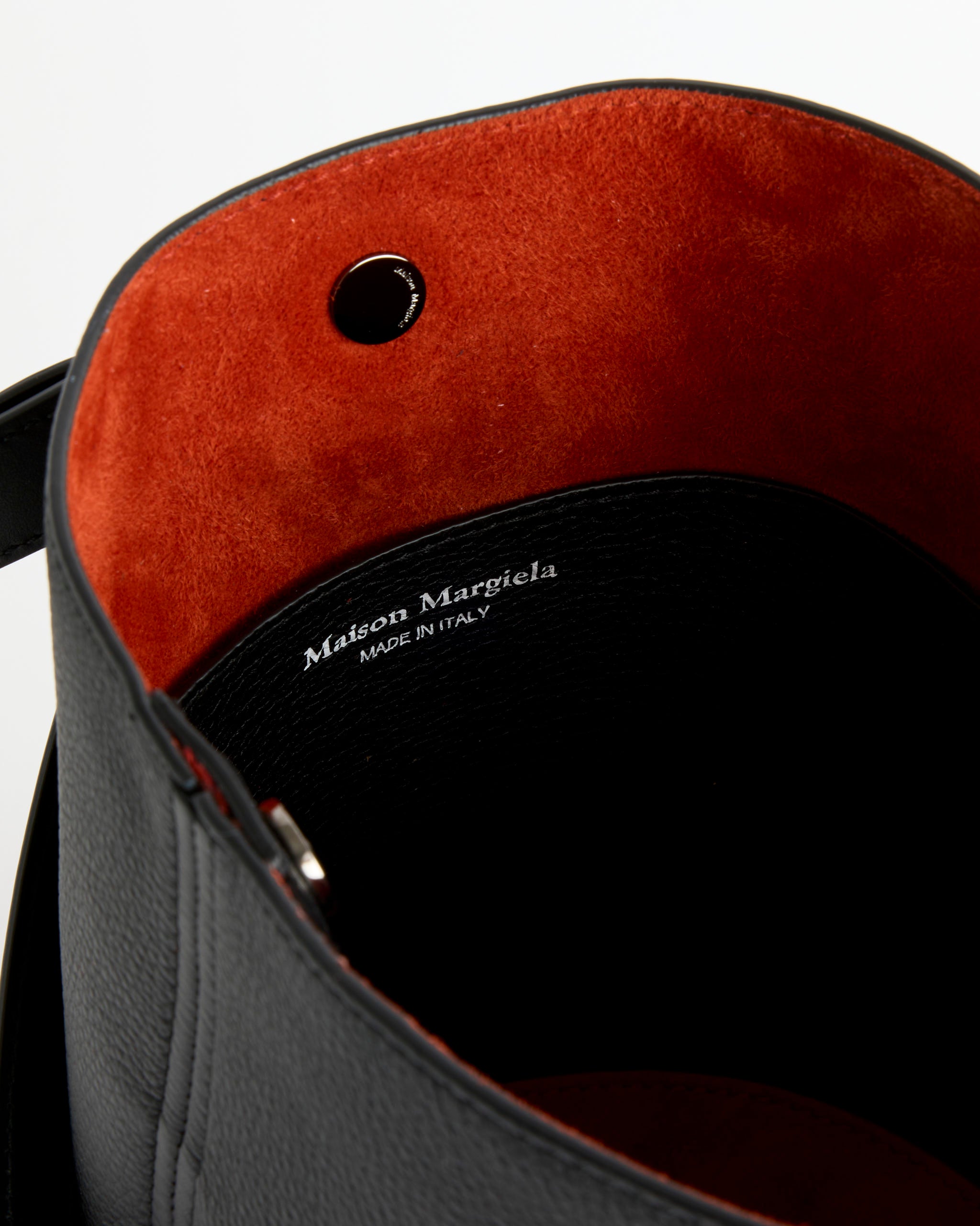 Close-up of the black pebbled calfskin Maison Margiela Dress-Age Hobo Bag’s interior with red suede lining, metal grommet, and the brand name plus ‘Made in Italy’ stamped in white.