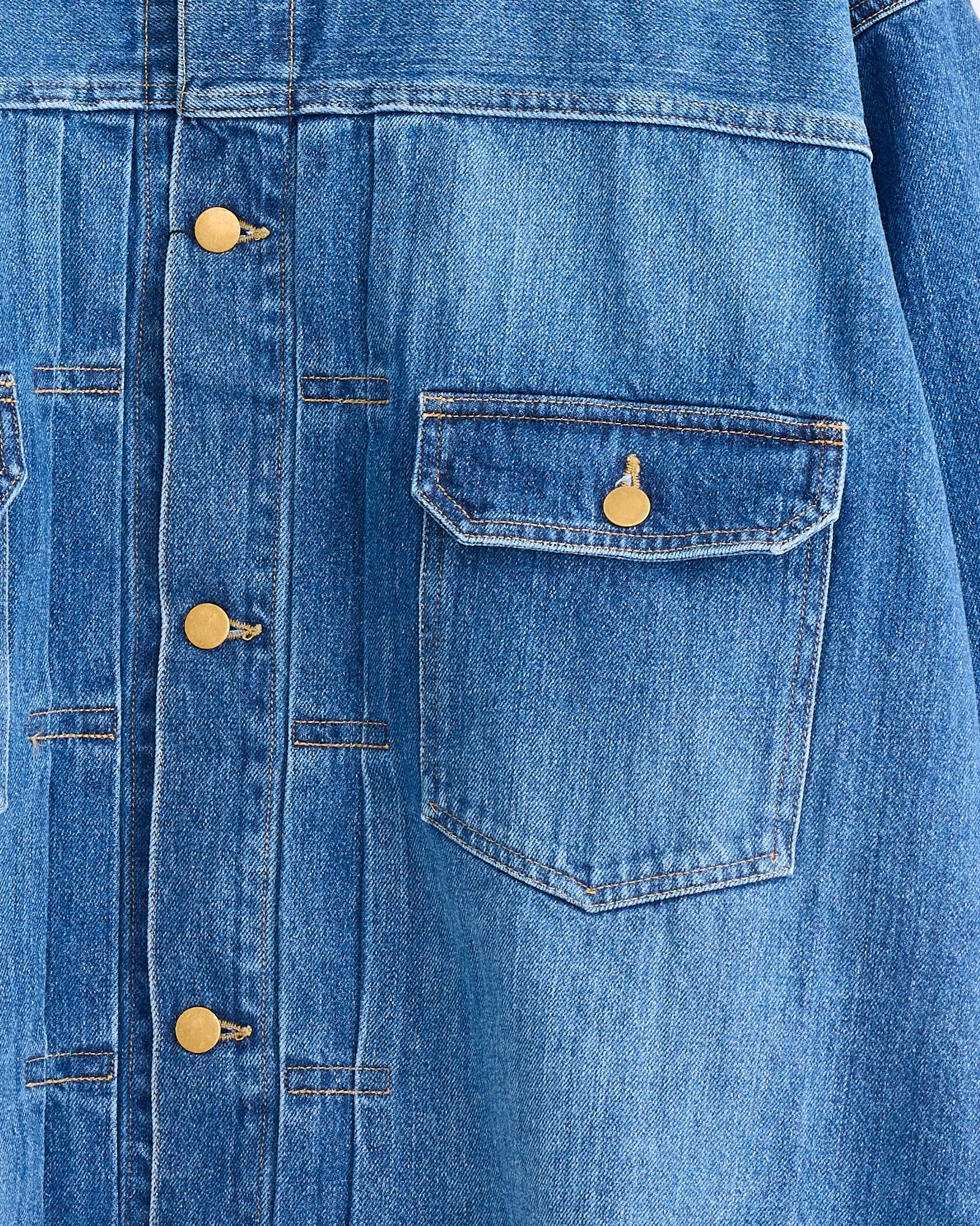 Close-up of the Sillage Trucker Jacket in Blue Denim Damaged, showing brass buttons, a front pocket with flap and button closure, and visible stitching highlighting the textured Made in Japan denim.