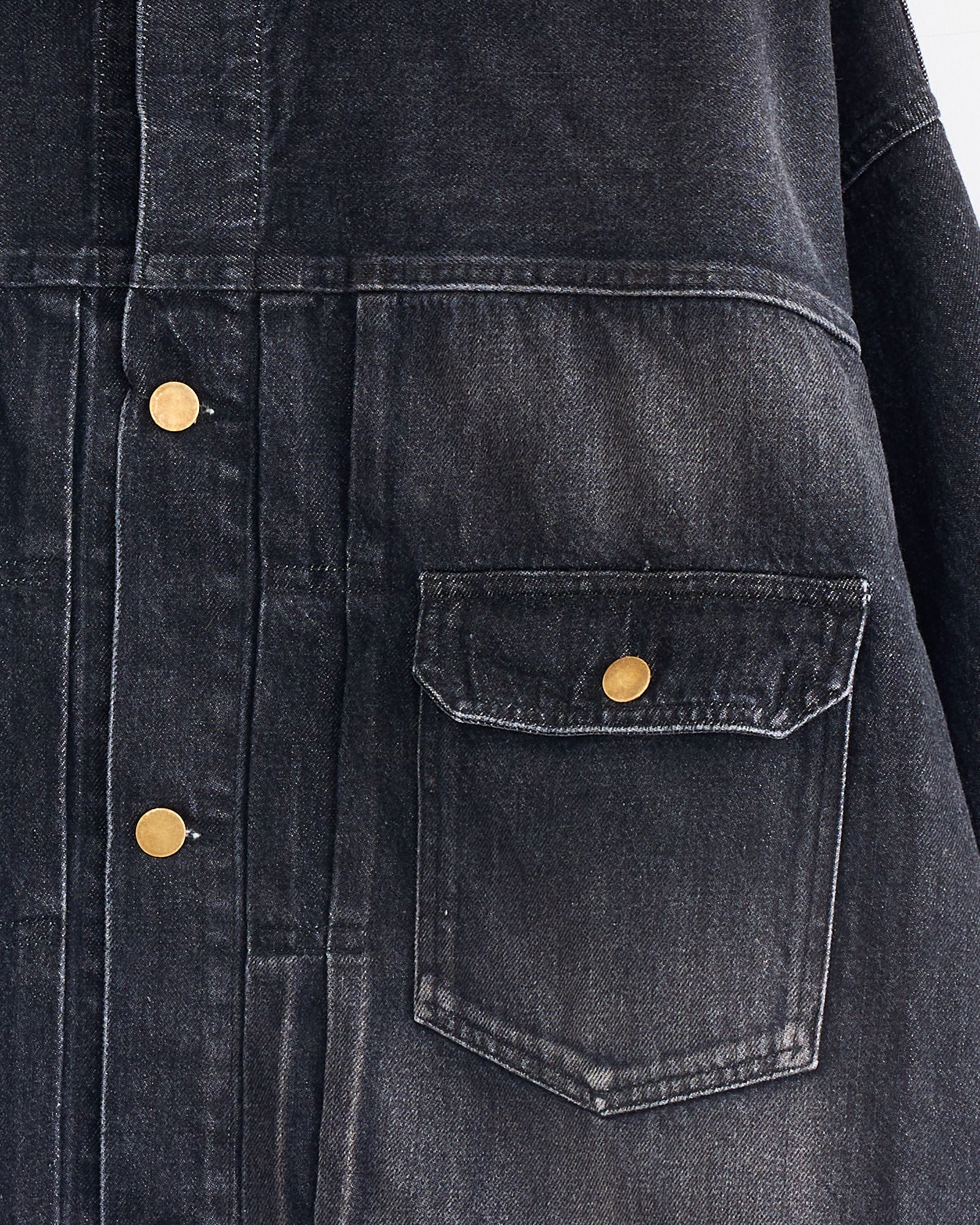 Close-up of the Sillage Trucker Jacket in Black Denim Damage, featuring gold metal buttons and a right front flap pocket. The visible texture and stitching showcase the jacket’s quality craftsmanship.