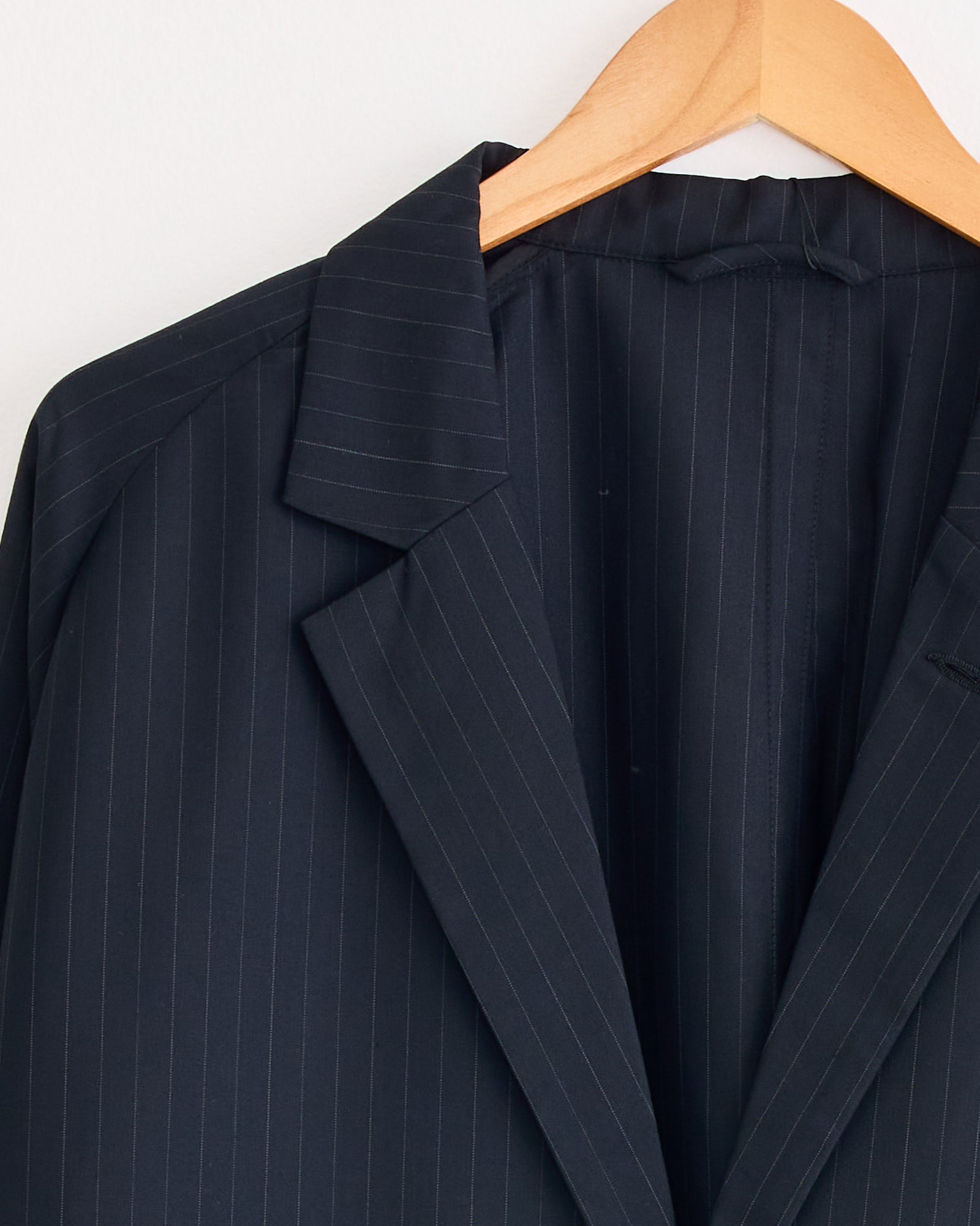 A close-up of the Sillage Veste Tropical Wool Two Button Jacket in Black Stripe, displayed on a wooden hanger, highlighting its collar and lapel against a white background.