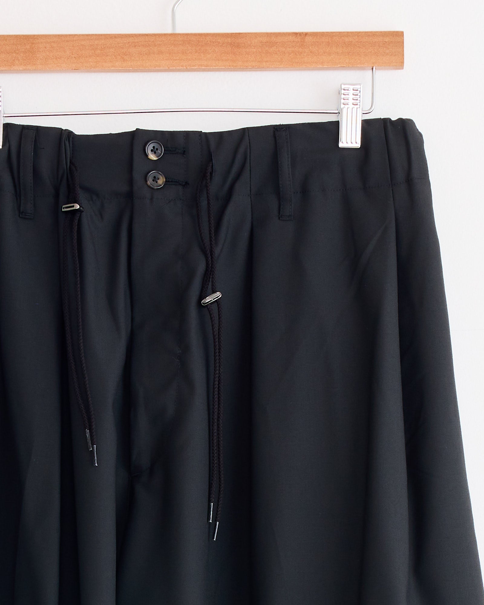 The Sillage Circular Tropical Wool Pant in Black features an elastic waistband with black drawstrings, two front buttons, belt loops, and a voluminous silhouette inspired by the brand's signature design.