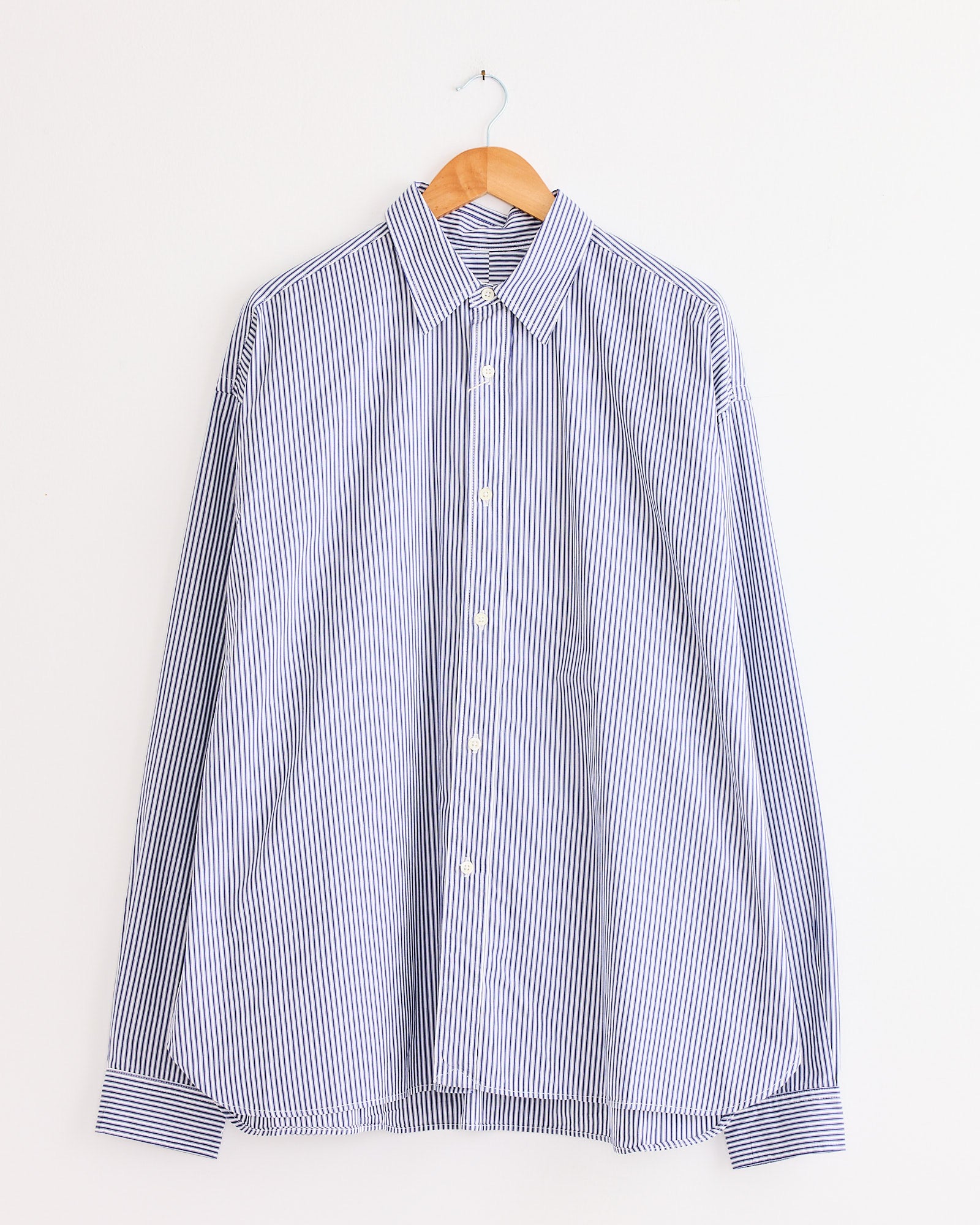 The Sillage Regular Wide High Count Shirt in navy stripe hangs on a wooden hanger against a plain white background.
