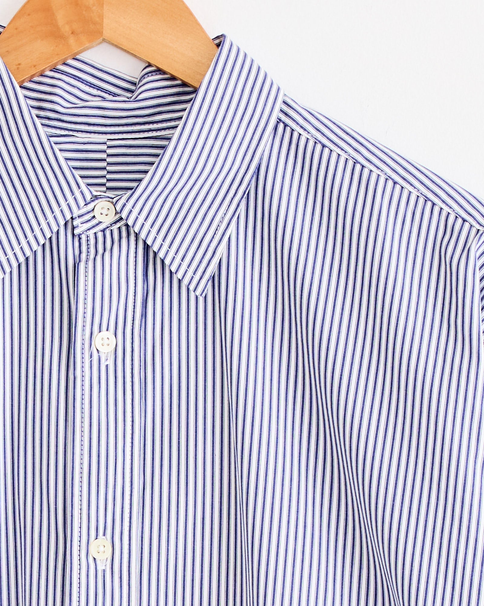 A close-up of the Sillage Regular Wide High Count Shirt in navy stripe, displayed on a wooden hanger against a white background.