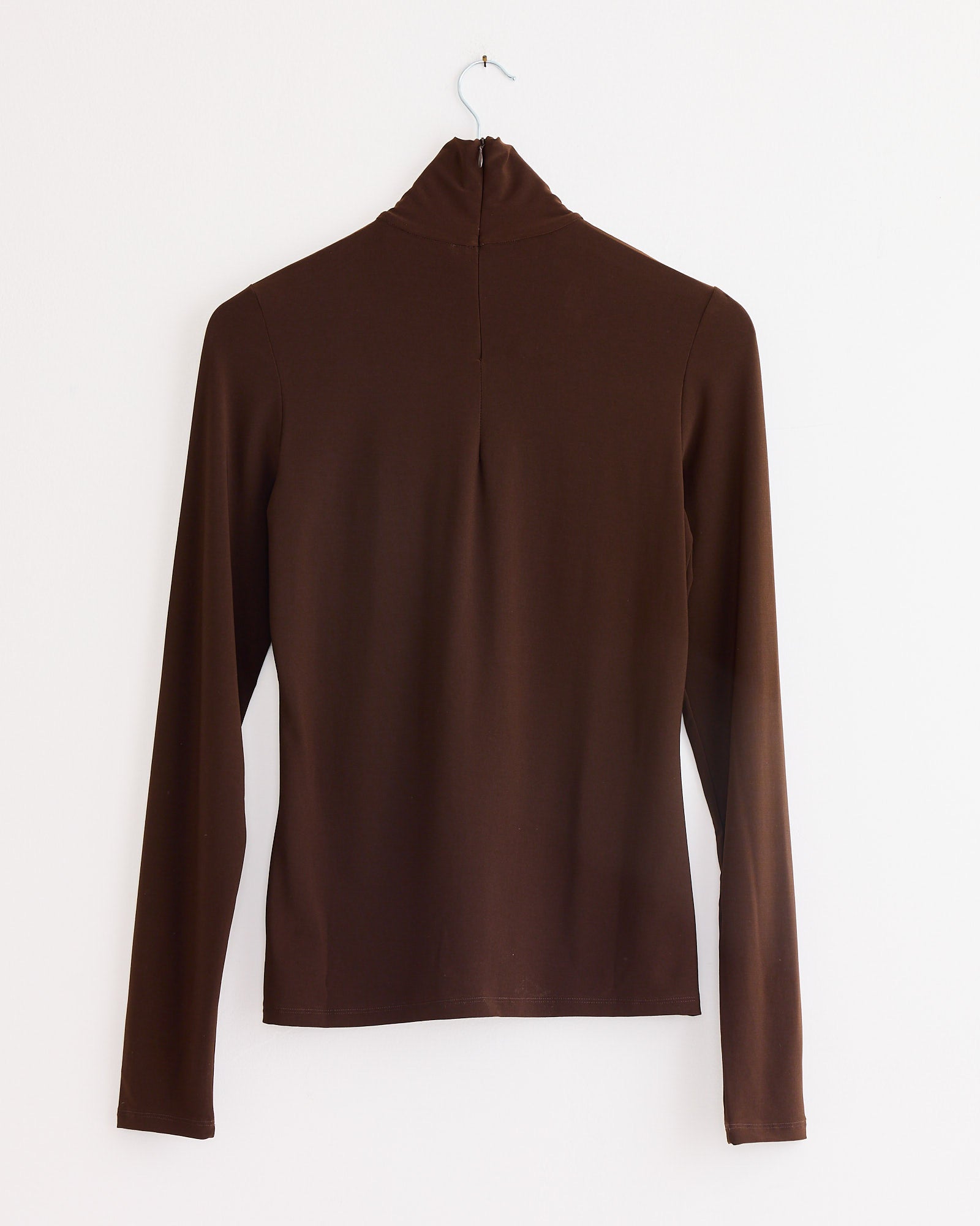 The Beaufille Button Down Rodin Blouse in brown, featuring a slim fit, is displayed on a silver wire hanger against a plain white wall, shown from the back.