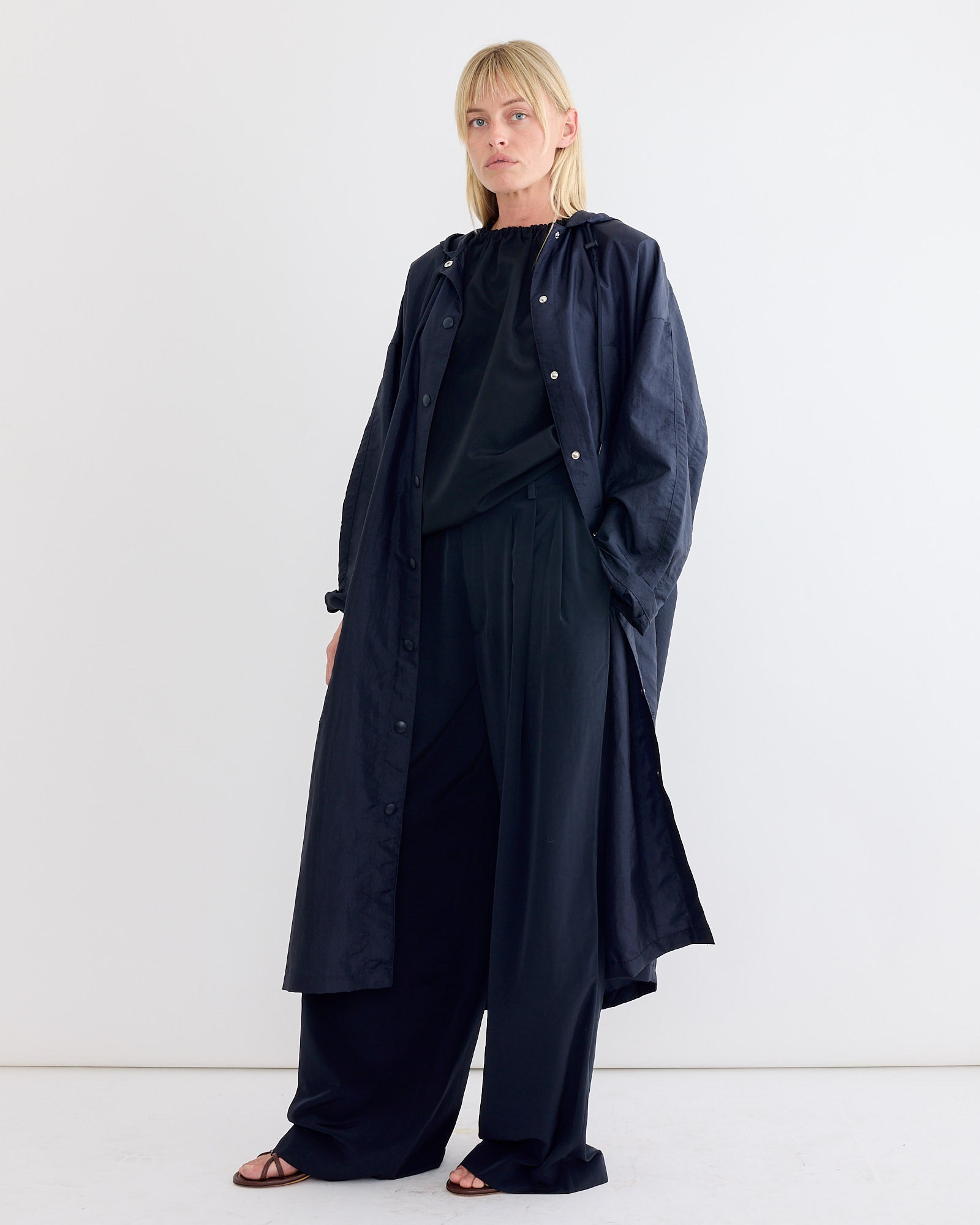 A woman in black clothes, styled with the Tibi Crispy Nylon Hooded Coat in Navy.
