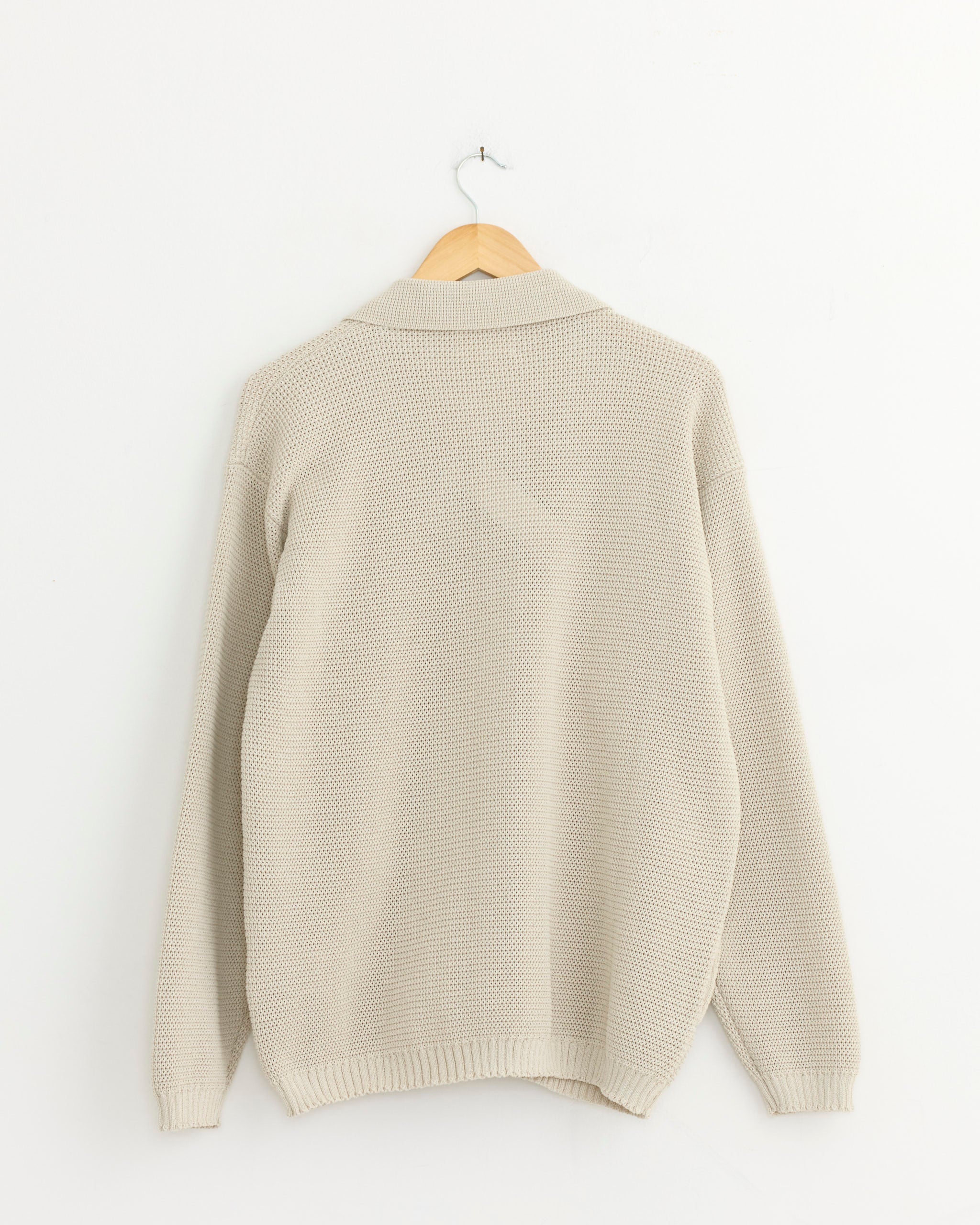 The Still By Hand Paper Mixed Knit Blouson in Taupe hangs on a wooden hanger against a white wall, highlighting the distinctive texture of Japanese paper yarn from the back.