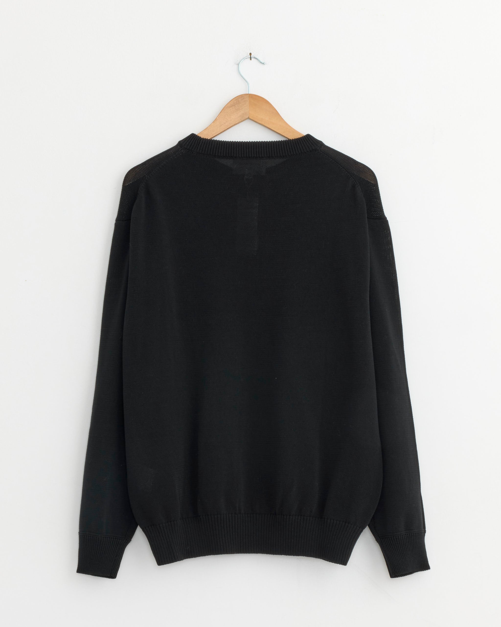 The Still By Hand 10g Cotton Sweater in Dark Charcoal is shown from the back on a wooden hanger against a white wall. Crafted in Japan for superior quality and timeless style.