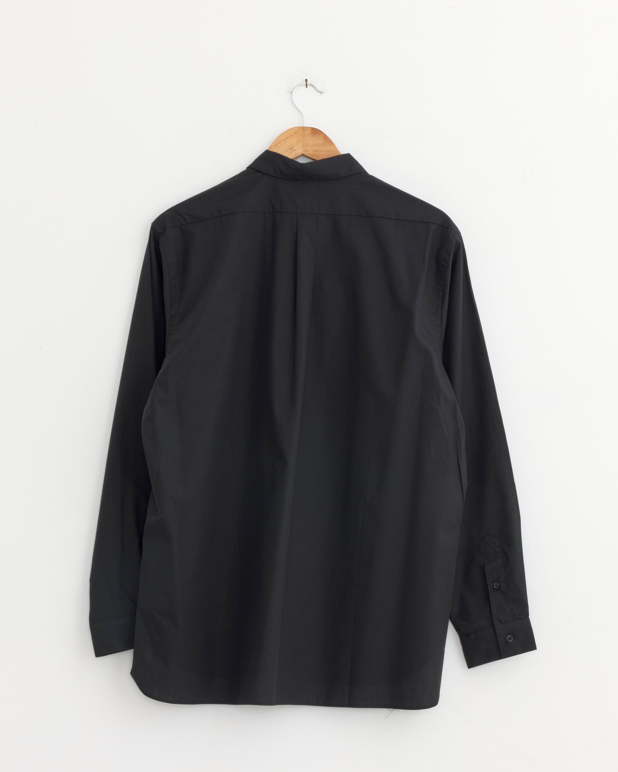 A Regular Collar Shirt in Navy Stripe by Still By Hand hangs on a wooden hanger against a plain white wall, shown from the back.