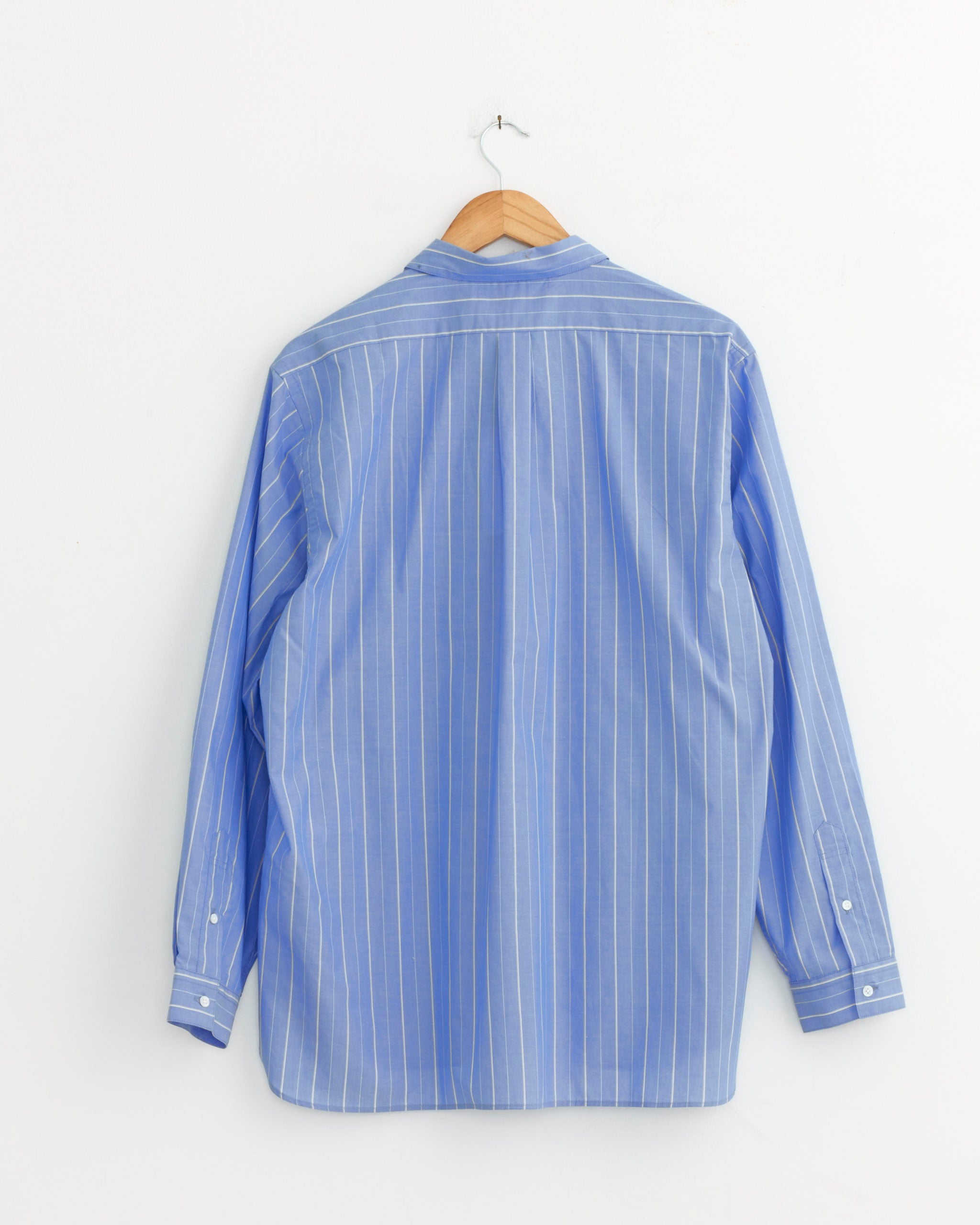 The Still By Hand Regular Collar Shirt in Blue Stripe, featuring white vertical stripes, is made in Japan and displayed from the back on a wooden hanger against a white wall.