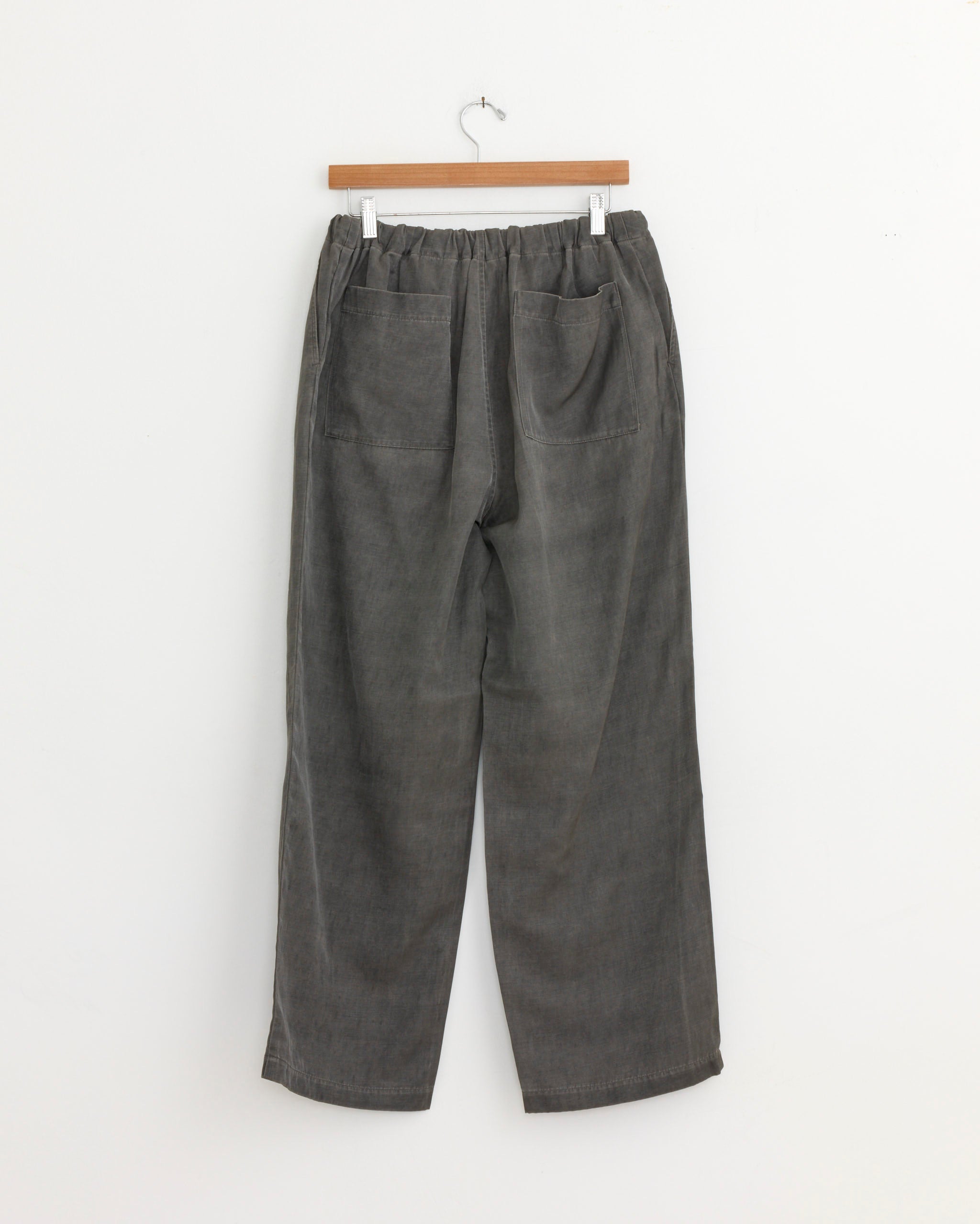 The Pigment Print Easy Pant in Dusty Grey by Still By Hand, made in Japan, features loose-fitting, high-waisted corduroy with an elastic waistband and two large back pockets, shown hanging on a wooden hanger against a white background.