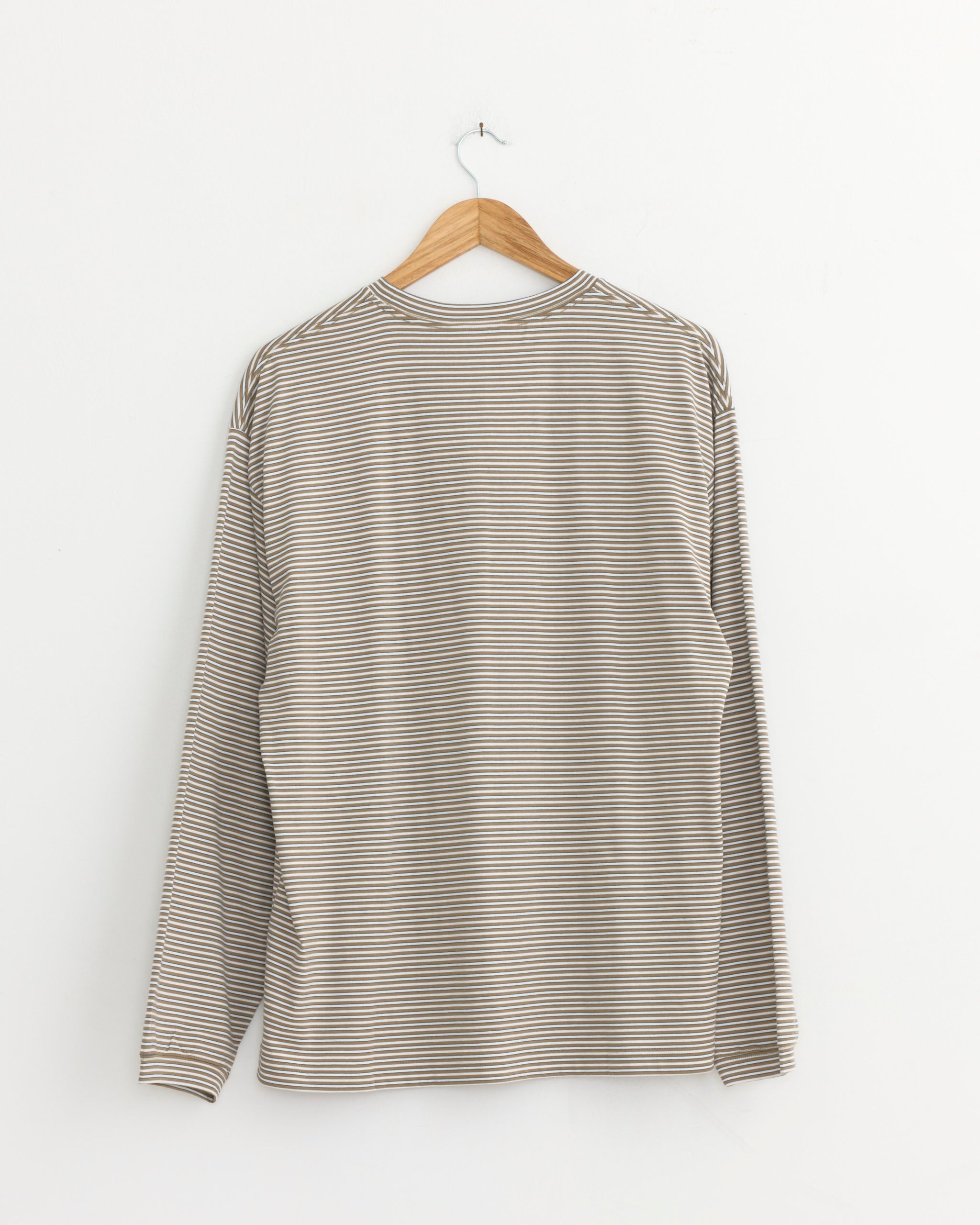 A Still By Hand Striped T-Shirt in Beige/White hangs on a wooden hanger against a plain white wall, displayed with the back facing forward. Made in Japan.