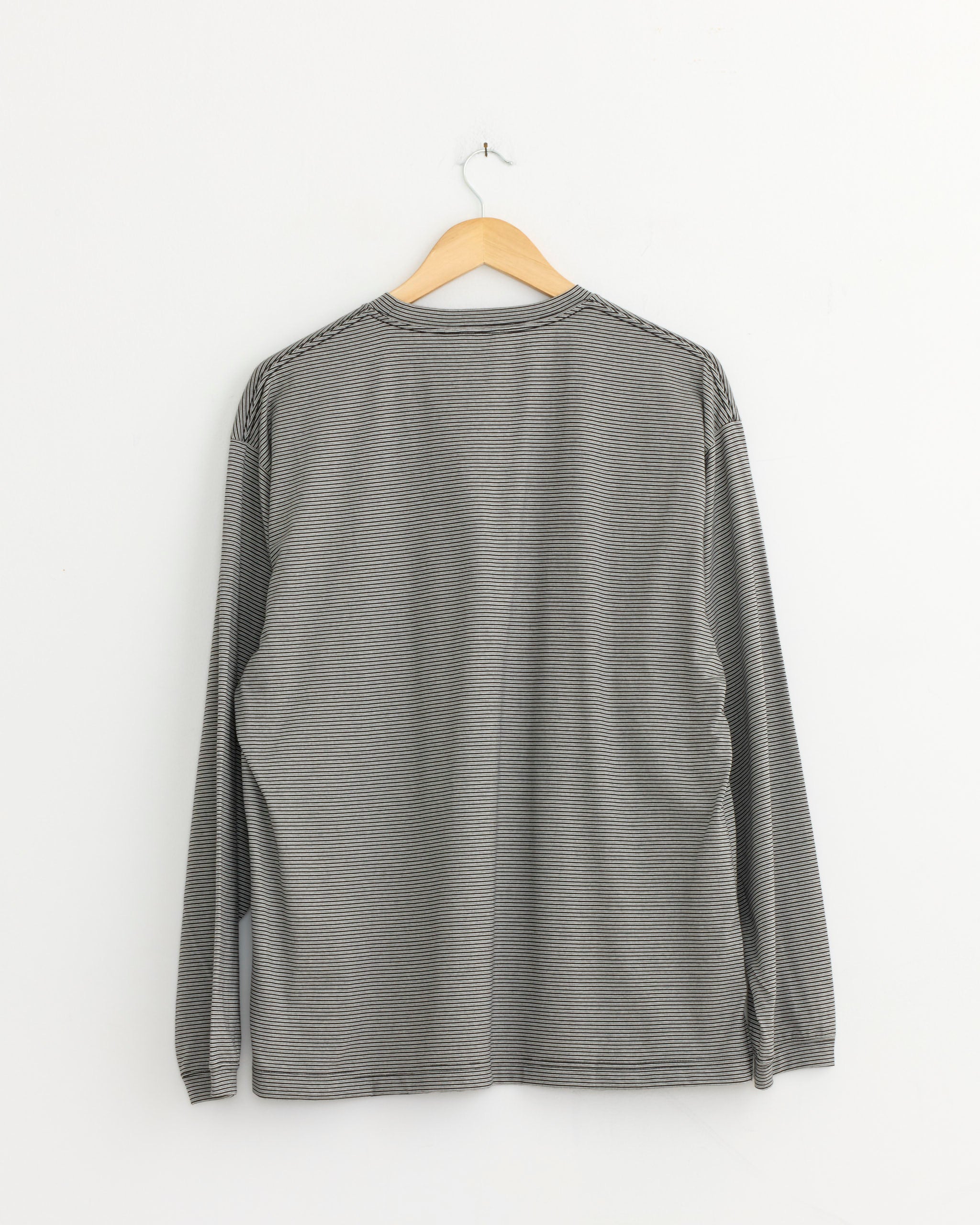 The Still By Hand Striped T-Shirt in Grey/Black with long sleeves is displayed from the back on a wooden hanger against a plain white wall. Made in Japan.