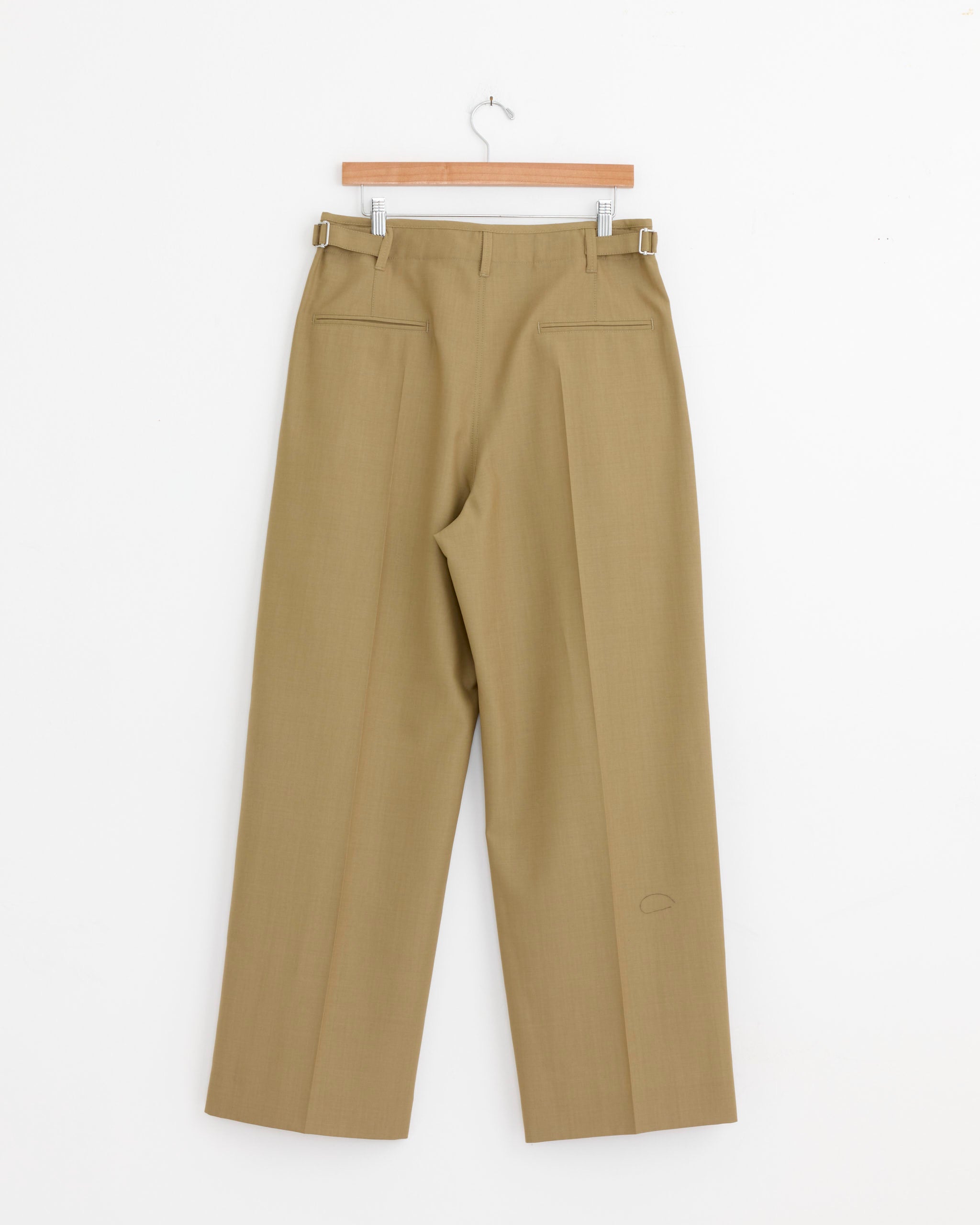 The Pleated Tailored Pant in Hay Green by Lemaire, a high-waisted, straight-leg khaki trouser in tropical wool suiting with front creases, hangs on a wooden hanger against a plain white background.