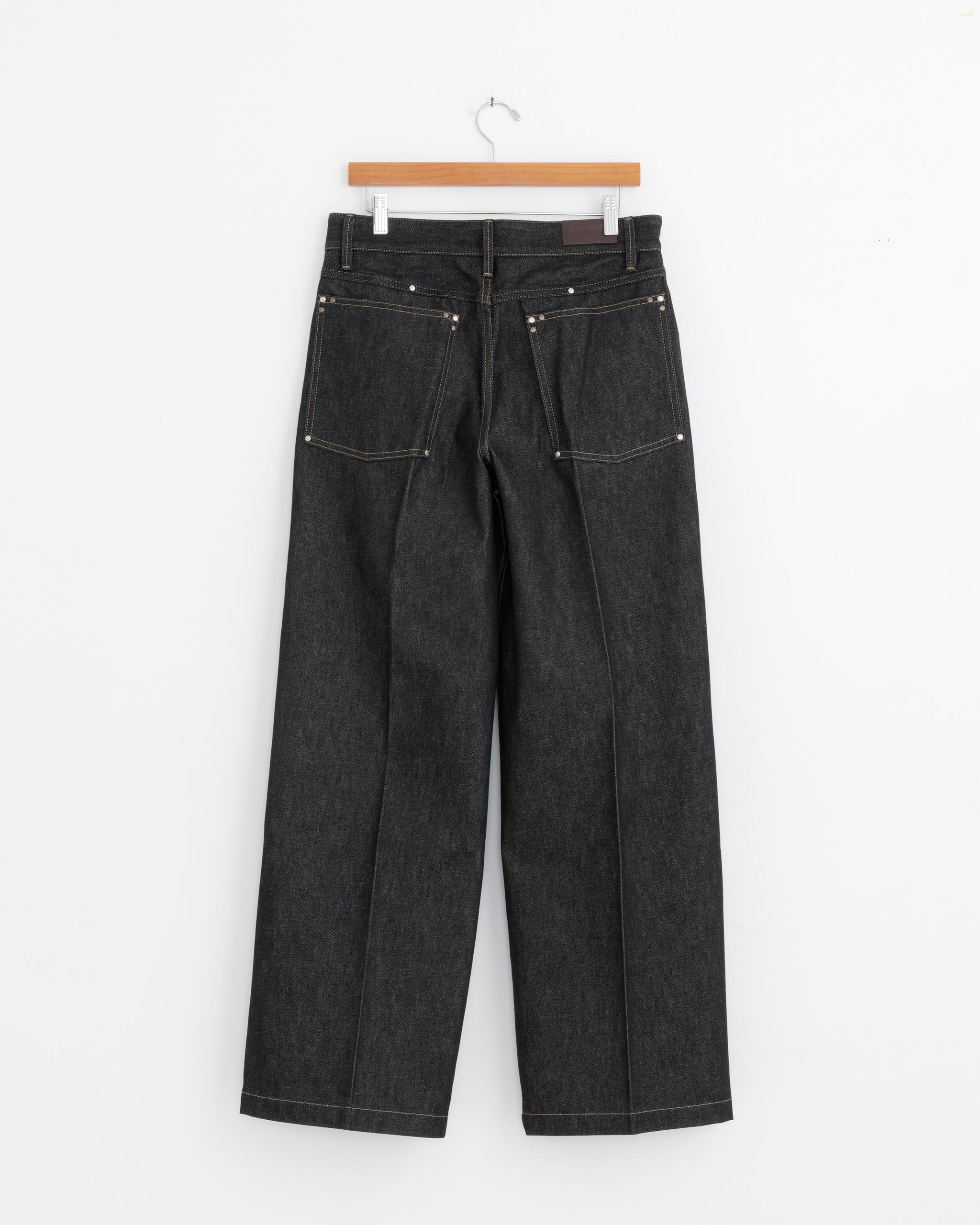 The Lemaire Wide Stud Pant in Slate is displayed from the back on a wooden hanger against a white background, featuring visible pockets and wide, straight legs.