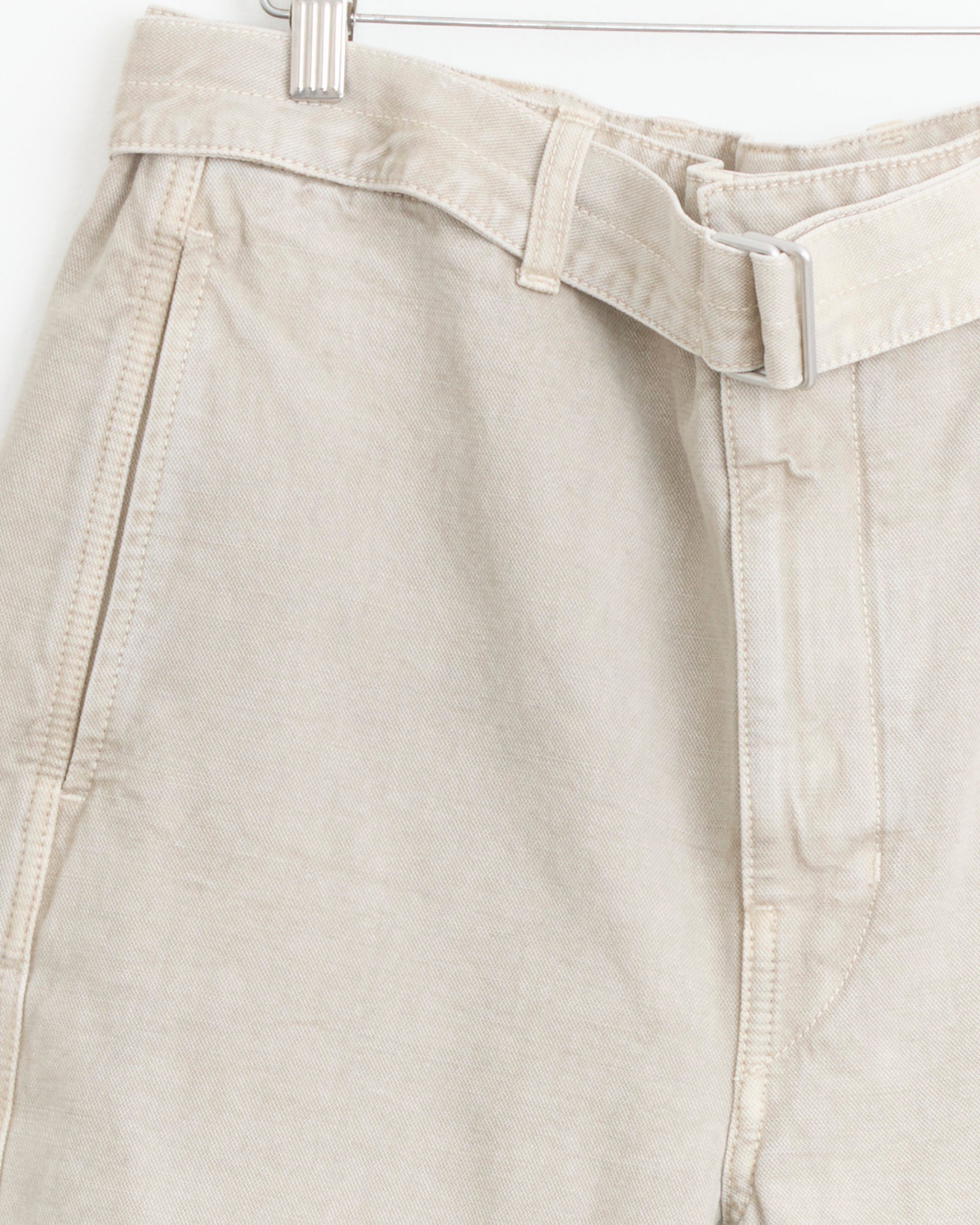 Close-up of Lemaire's Denim Short in Moonstone, featuring a classic Bermuda silhouette with a fabric belt, metal buckle, and visible stitching details, hanging on a hanger.