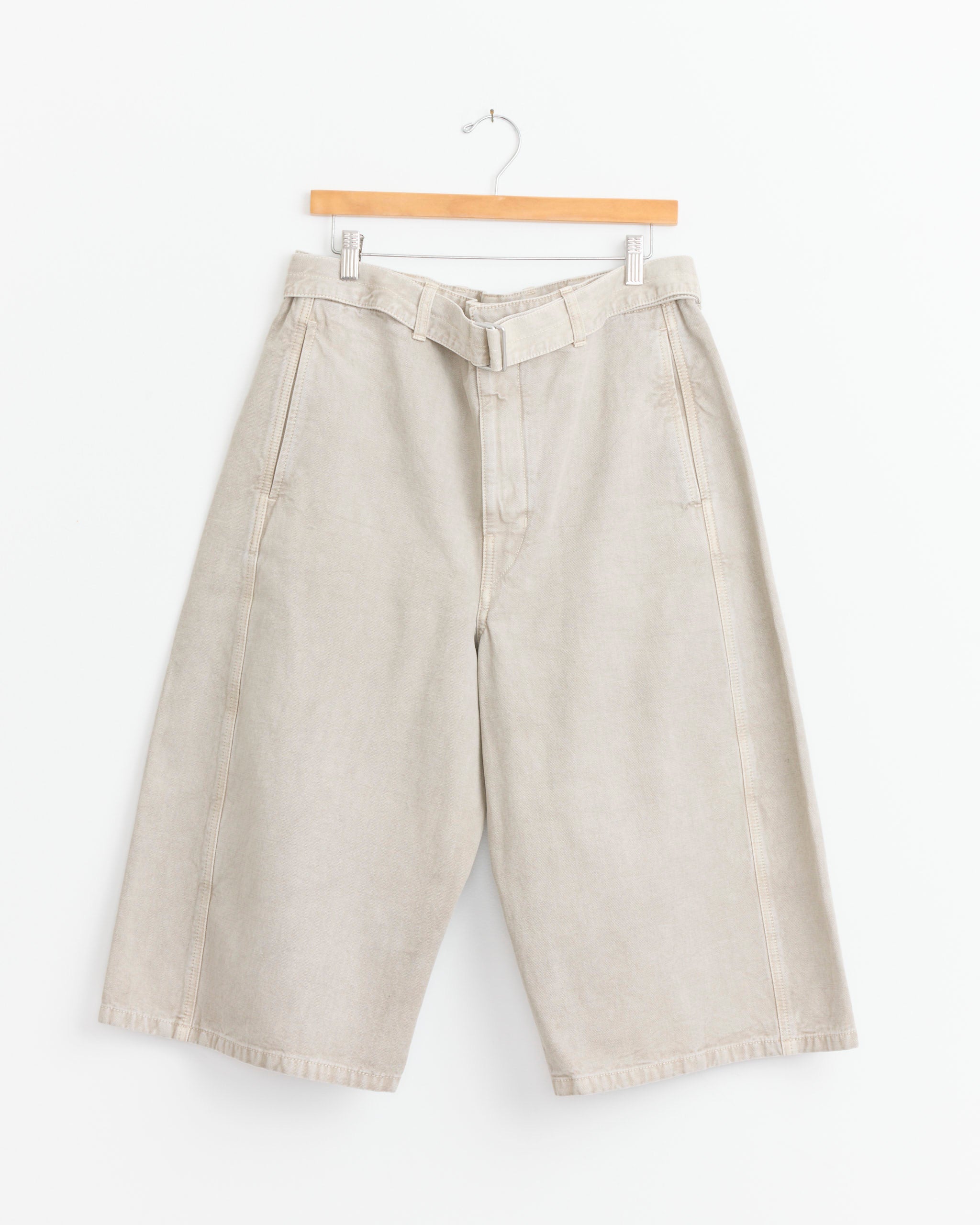The Lemaire Denim Short in Moonstone features a wide-legged Bermudas silhouette with a matching belt, shown hanging on a wooden hanger against a plain white background.