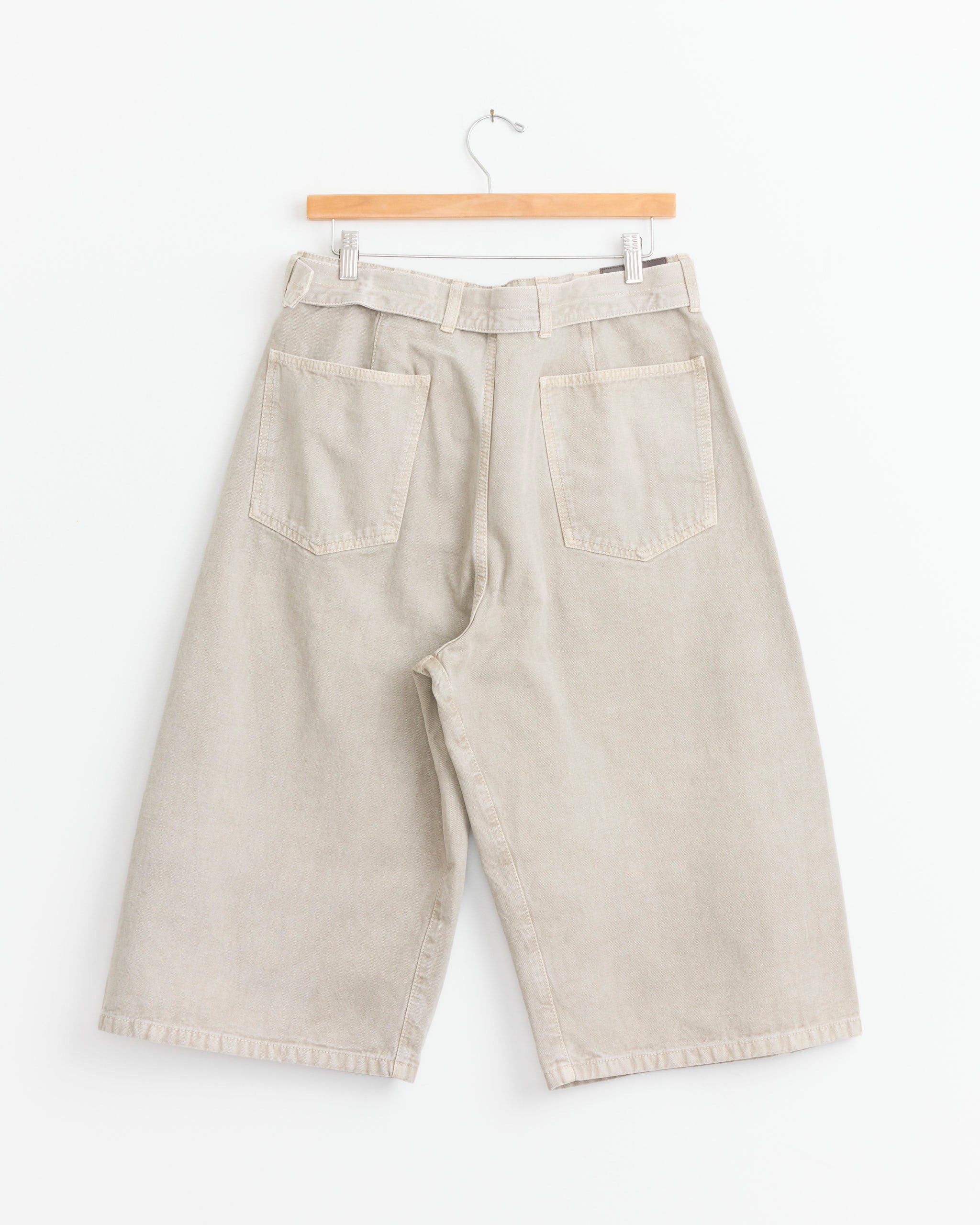 Lemaire Denim Short in Moonstone, featuring a relaxed bermuda silhouette and two back pockets, is shown hanging on a wooden hanger against a plain white background.