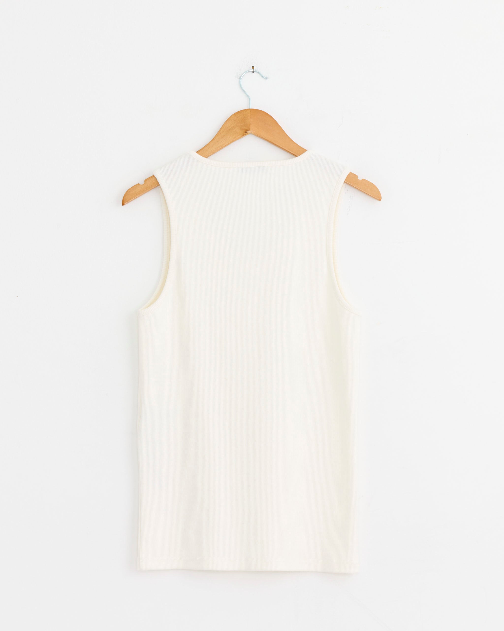 A Lemaire Rib Tank Top in Milk is displayed on a wooden hanger against a plain white wall, shown from the back.