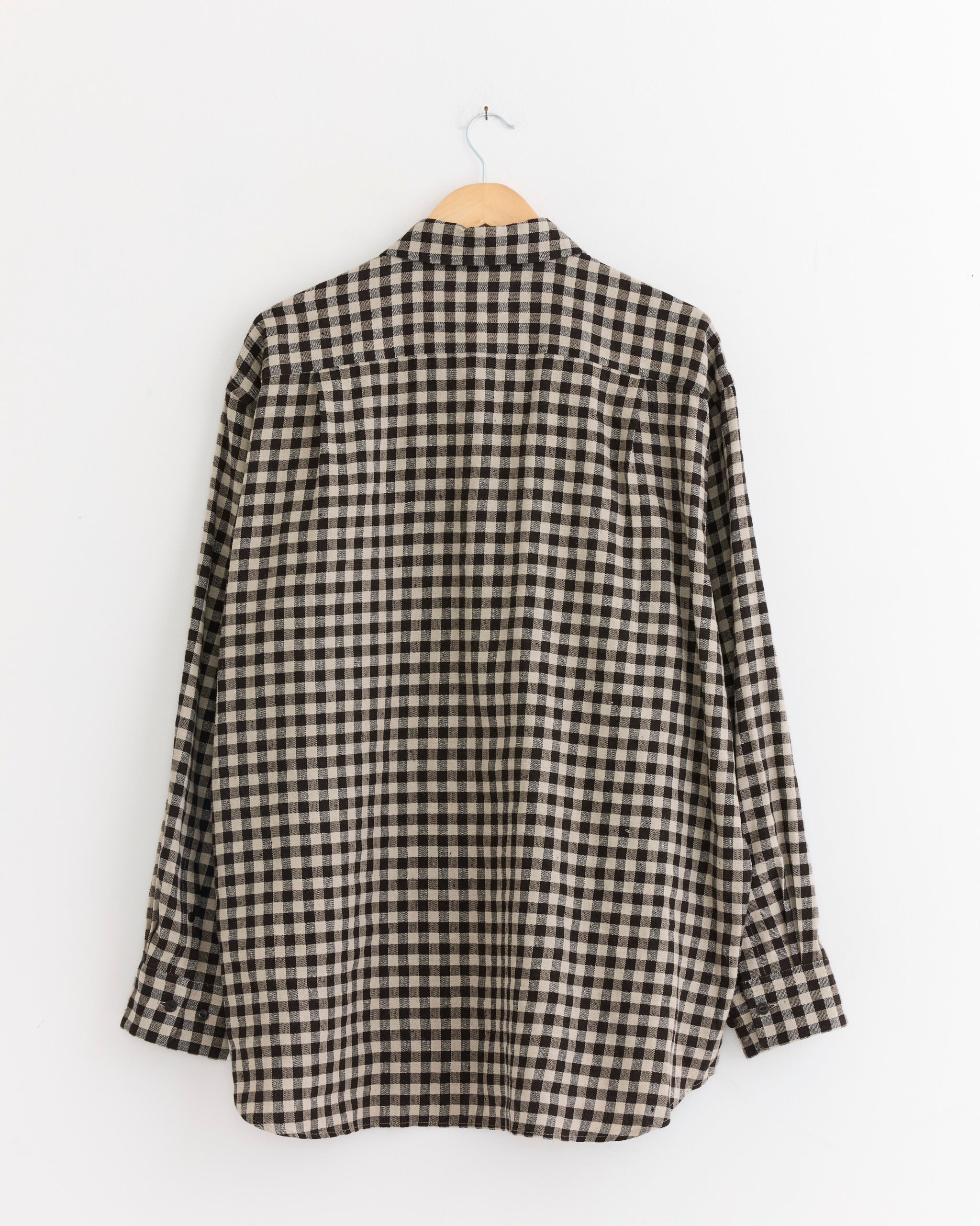 A black and white gingham Regular Collar Shirt by Yoko Sakamoto hangs on a wooden hanger against a white wall, shown from the back. Made in Japan.