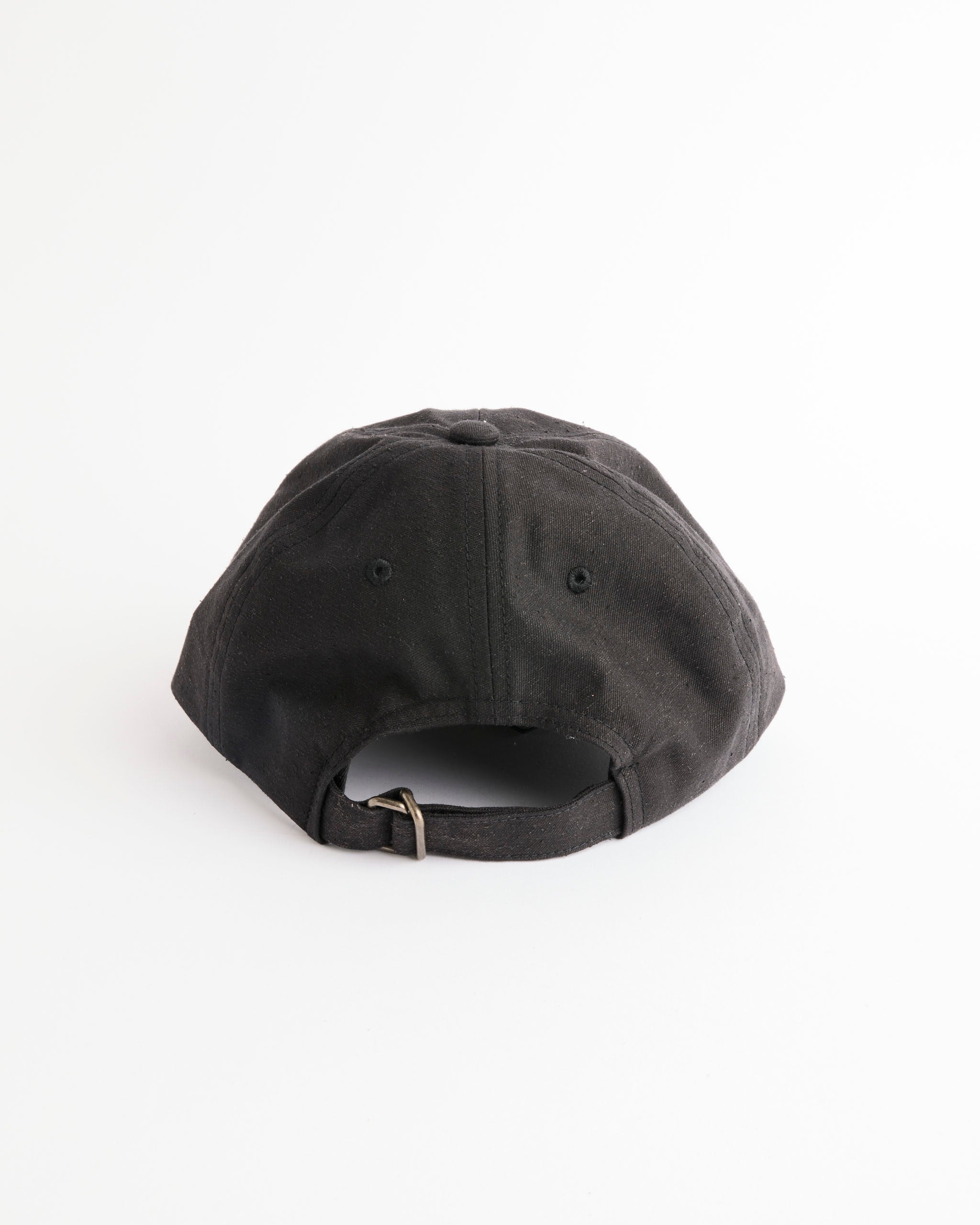 The Gift Shop Cap in Black by Yoko Sakamoto is shown from the back with an adjustable metal-buckle strap against a white background, evoking the classic style of a vintage souvenir cap.