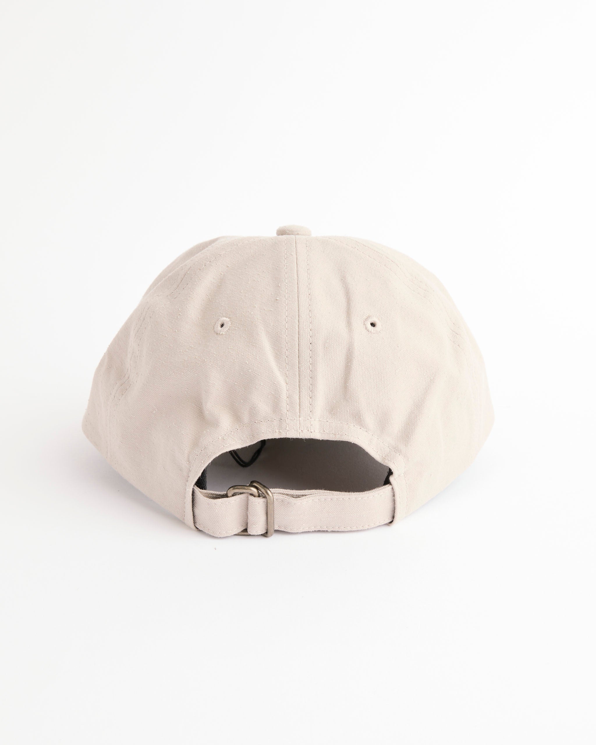 The Yoko Sakamoto Gift Shop Cap in Beige is a six-panel cap shown from the back, featuring an adjustable metal buckle strap and crafted from a soft cotton-silk blend, set against a plain white background.
