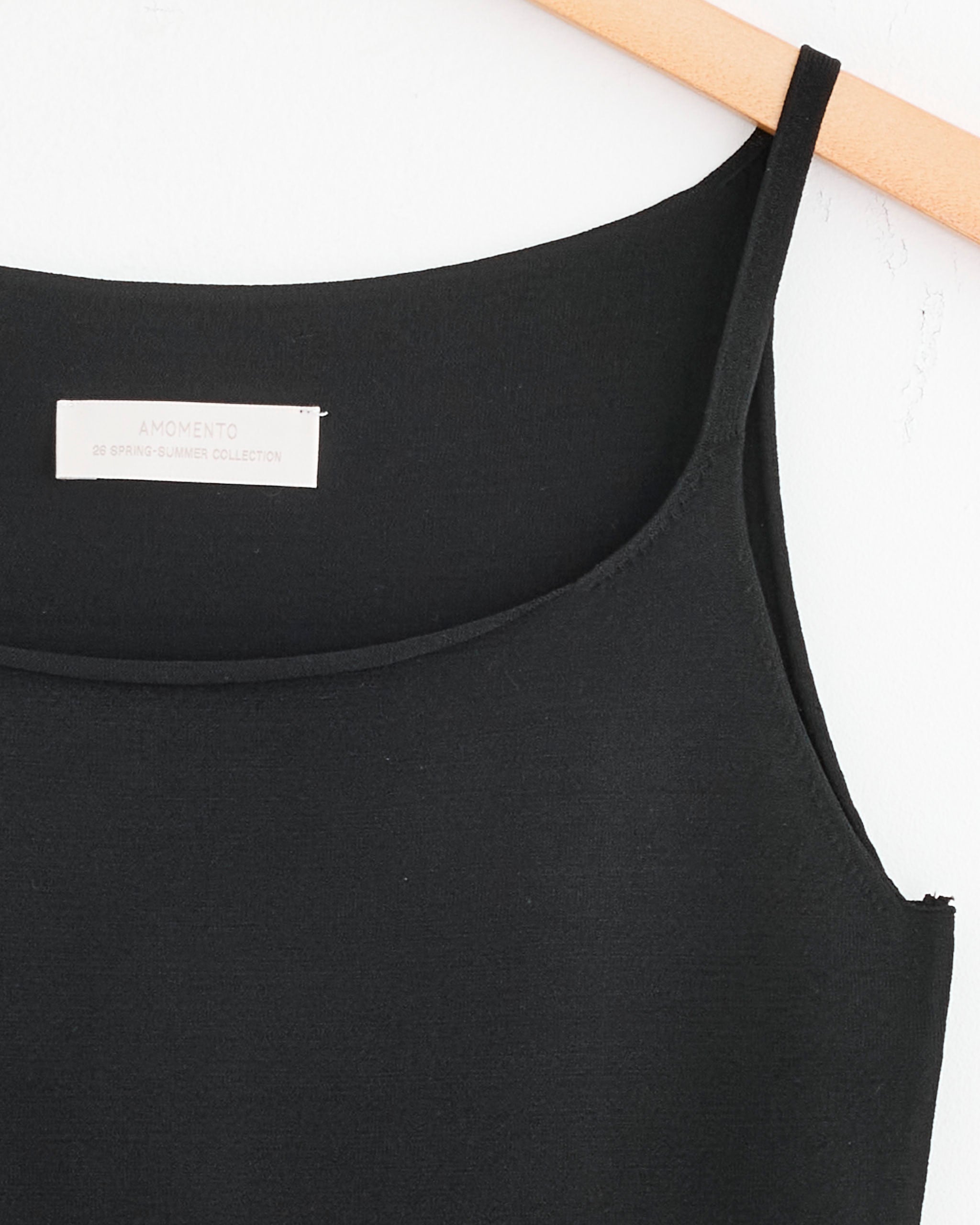 A close-up of the Amomento Sleeveless Knit Top in Black with thin straps, displayed on a wooden hanger.