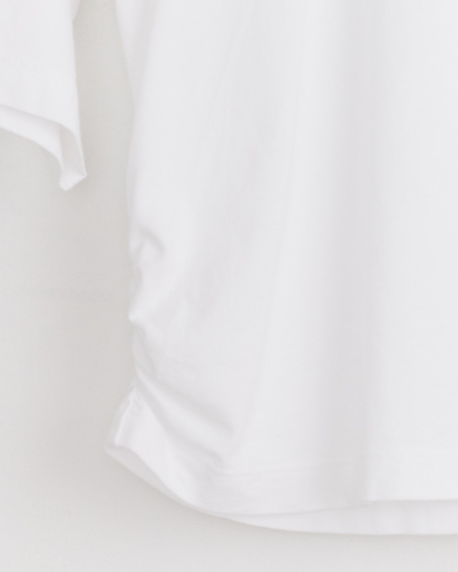 A close-up of the AGOLDE Shari Tee in White hangs against a white background, with only part of the shirt visible—ideal for viewing its sizing and fit before purchase.