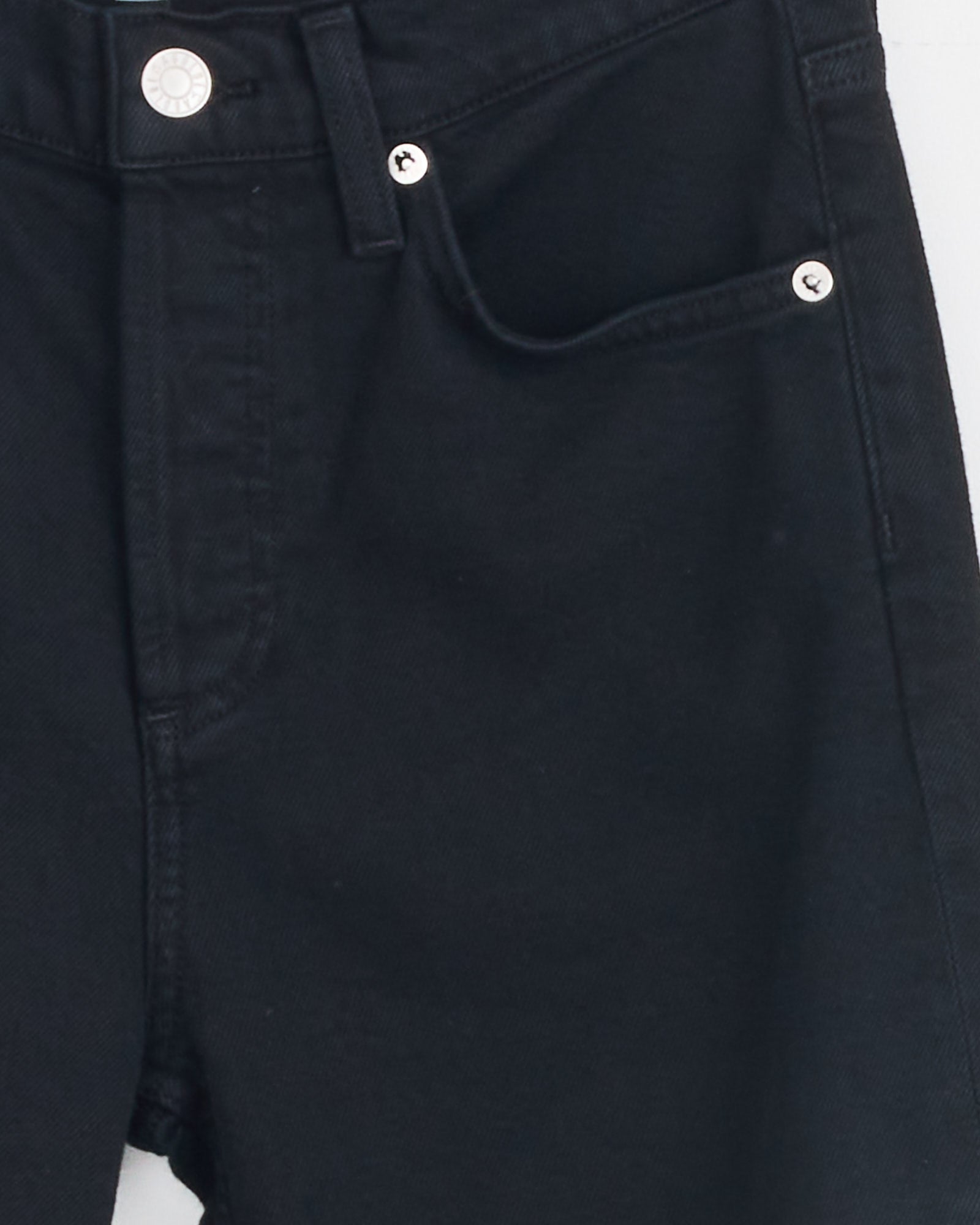 Close-up of the upper part of the AGOLDE Ingram Split Skinny in Immersion, highlighting the black denim waistband, button, zipper area, and front pocket with metal rivets. For fit or sizing questions, contact us via online chat.
