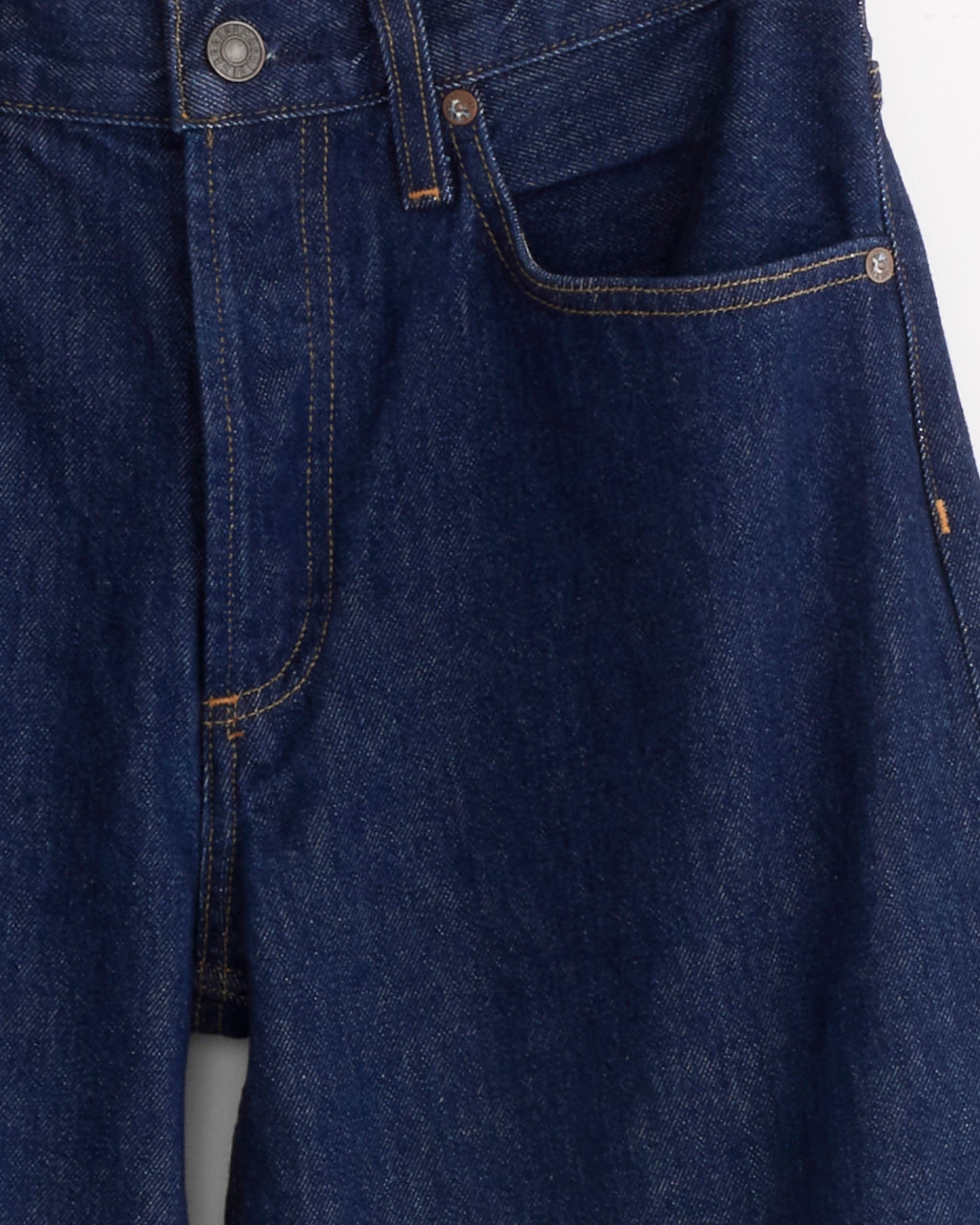 A close-up of AGOLDE’s Arc Jean 32" in Rinse, crafted from regenerative cotton, highlights the waistband, front pocket, zipper area with visible stitching, and a metal button.